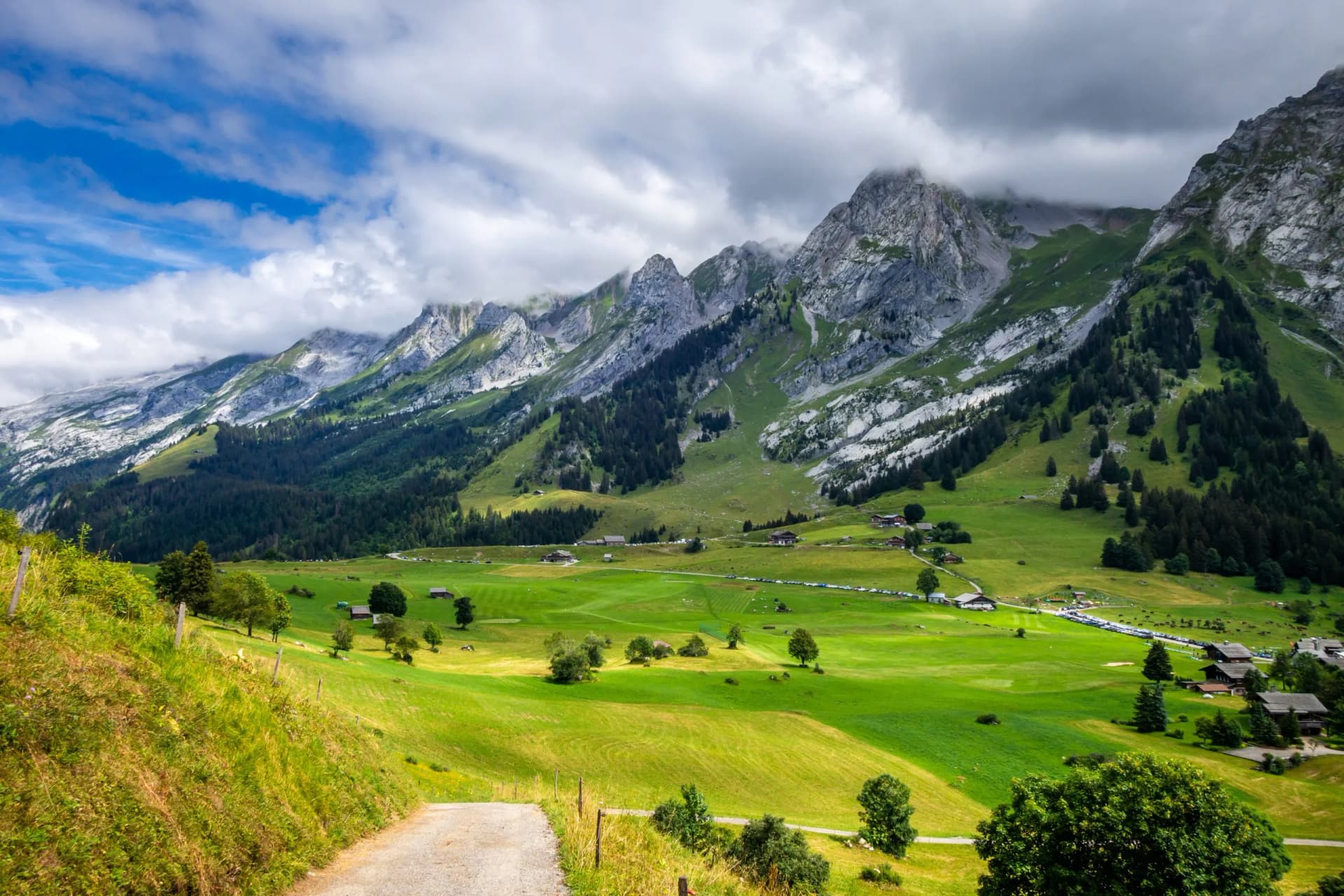 Aravis mountain range in Haute-Savoie, France, with green valleys and cloudy sky.