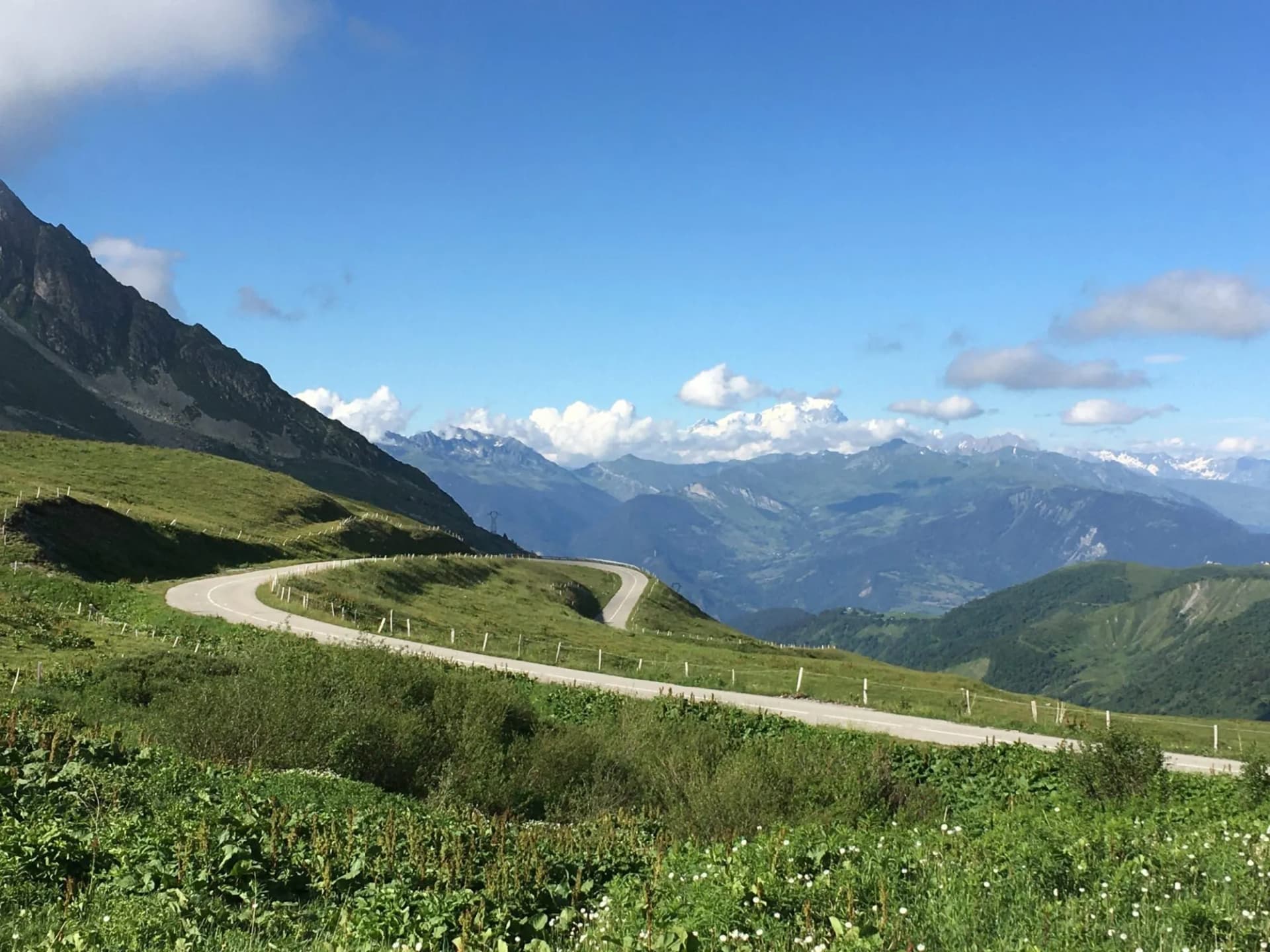 Winding mountain road at Col de la Madeleine in summer with green slopes and blue sky.