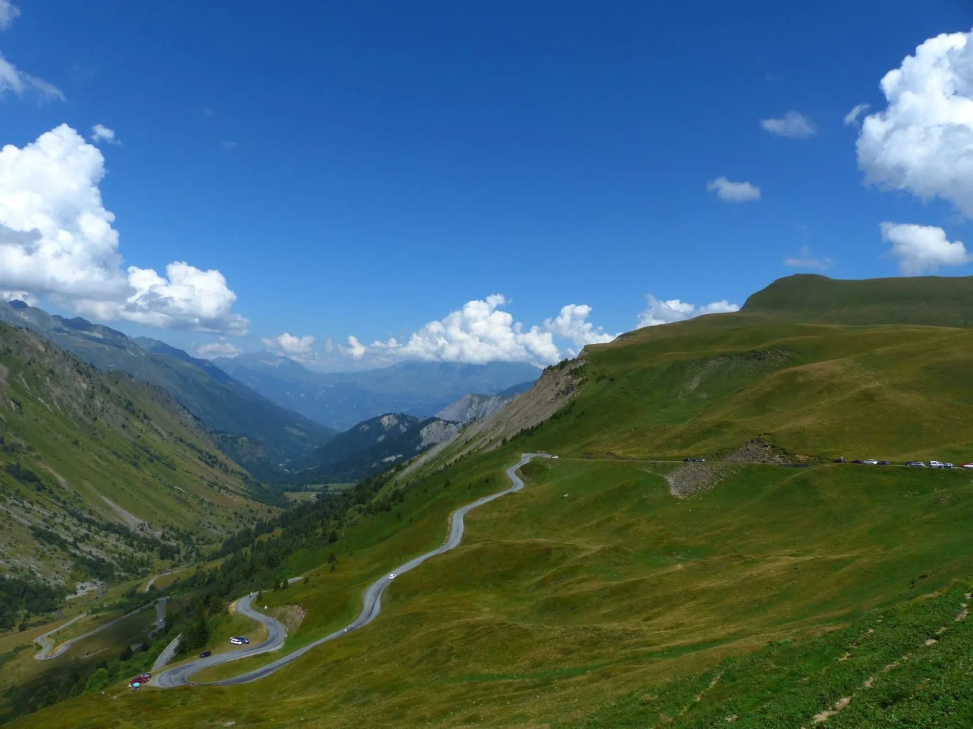 Winding mountain road with switchbacks in Savoie under a bright blue sky with clouds.