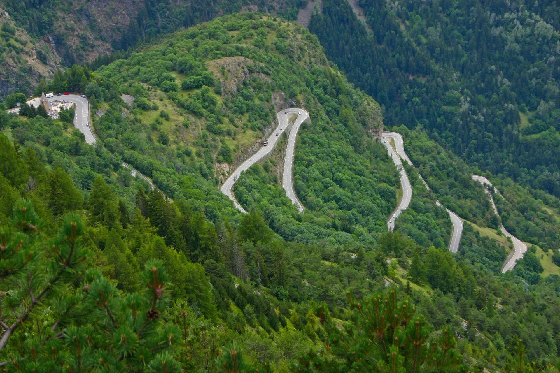 Winding mountain road hairpin curves ascending lush green slopes, Alpe d'Huez, France.