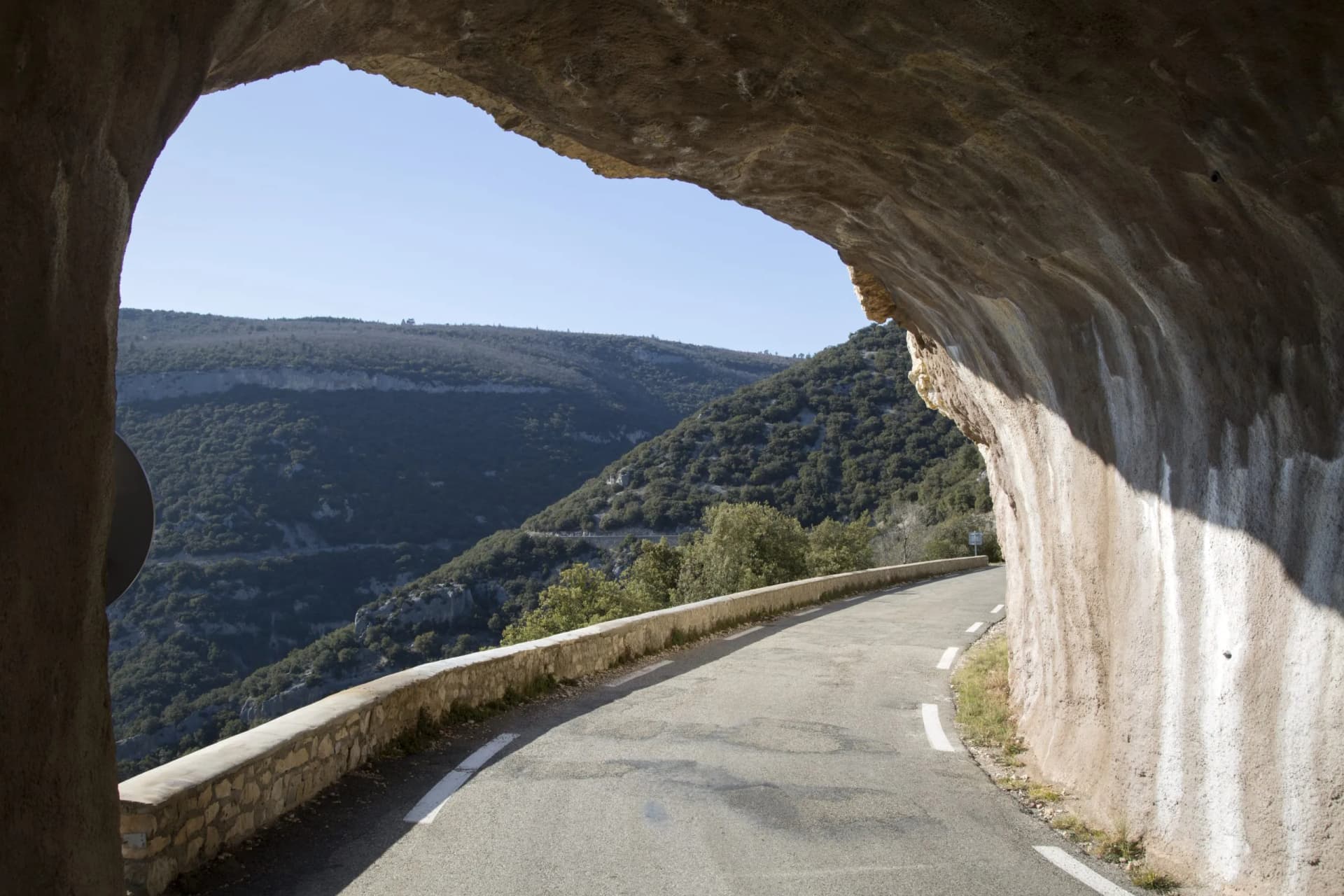 Road exiting a rock tunnel overlooking forested Gorges de la Nesque canyon pass, Provence, France.