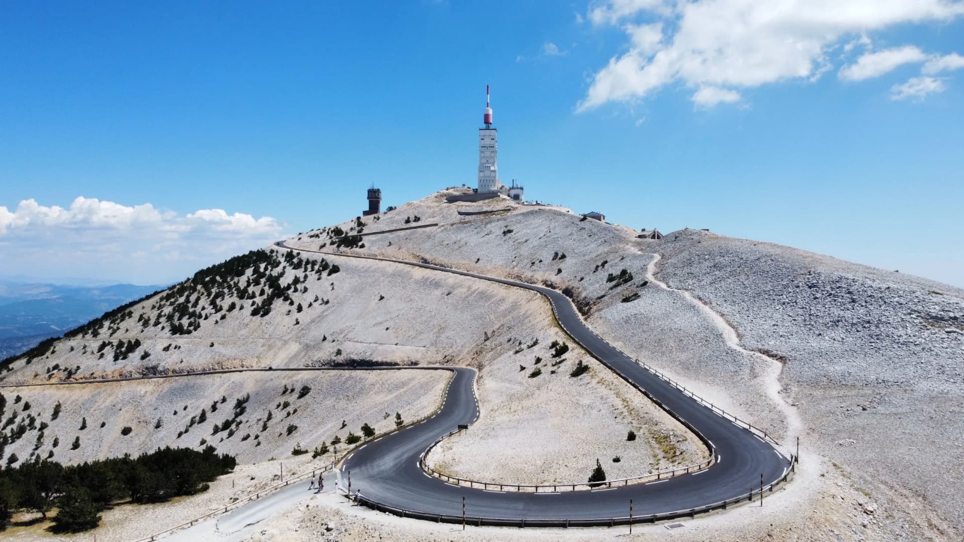 Winding road ascending Mont Ventoux in France with communication towers under a blue sky.