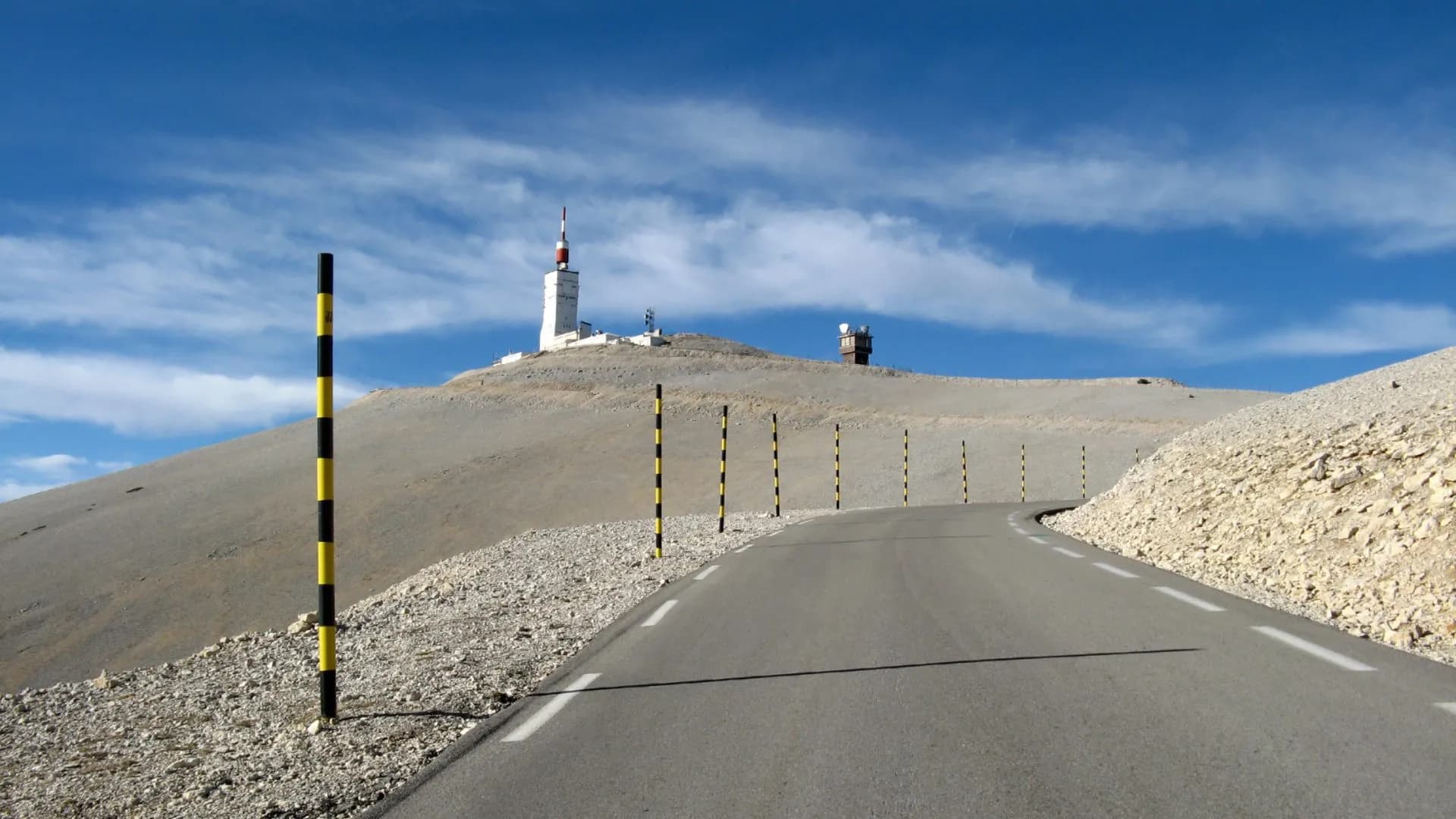 Winding road ascending barren Mount Ventoux toward summit observatory buildings, Vaucluse, France.