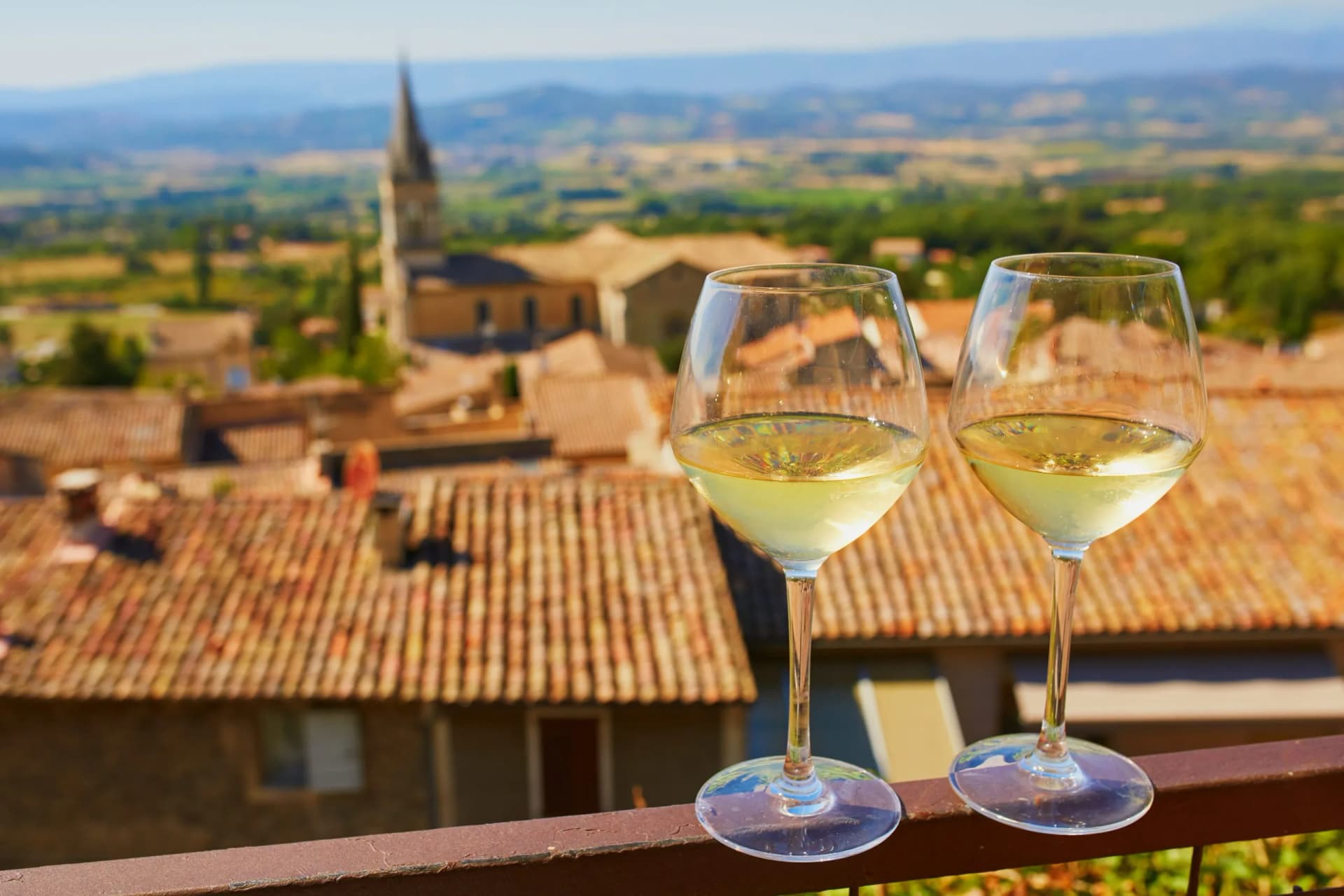 Two glasses of white wine overlooking terracotta roofs of Bonnieux village, Provence, France.