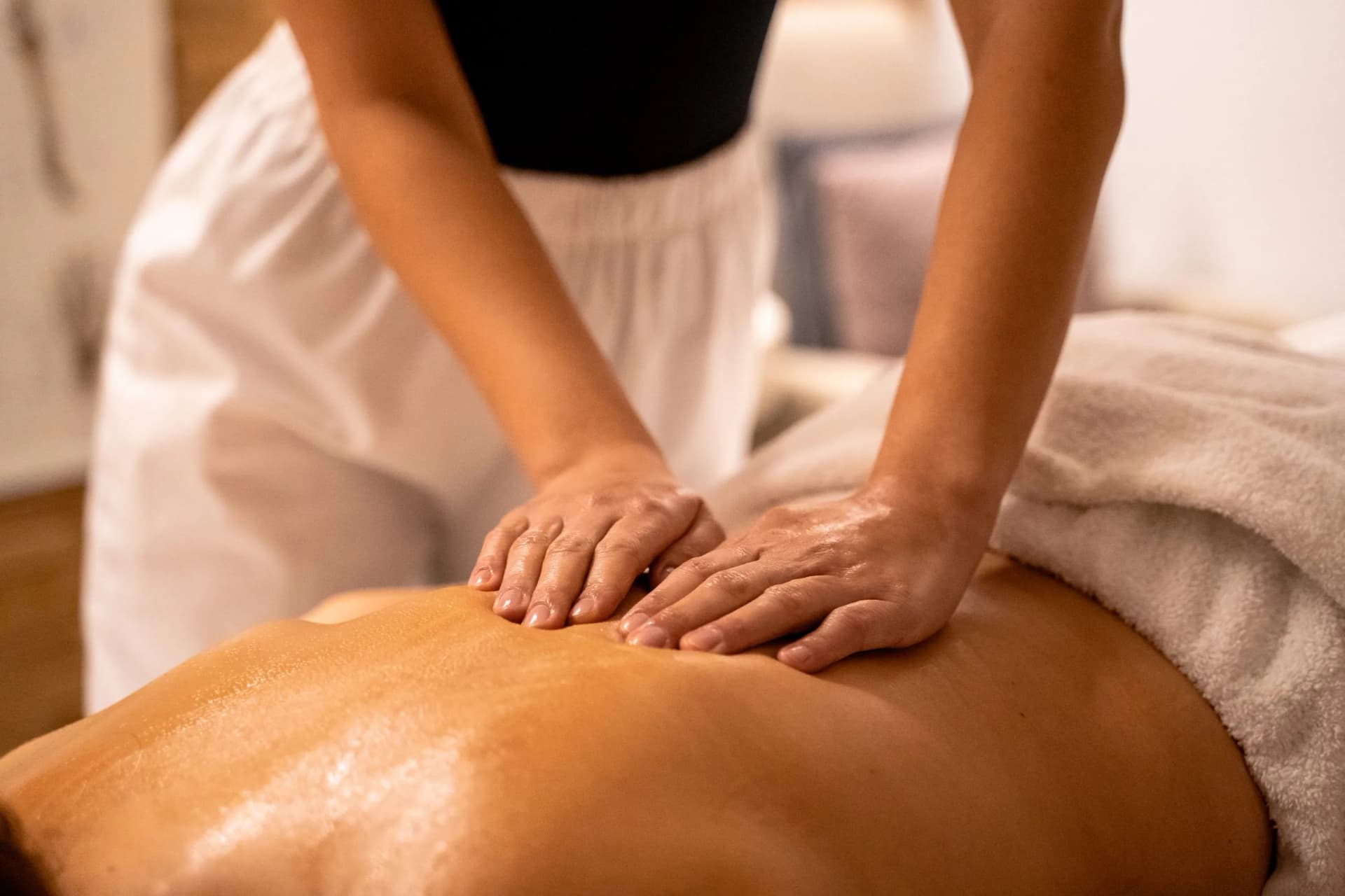 Close-up of hands applying oil to a person's back during a relaxing massage therapy session.