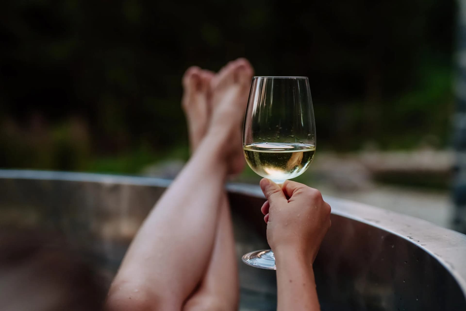 Woman relaxing with white wine in outdoor hot tub with nature background