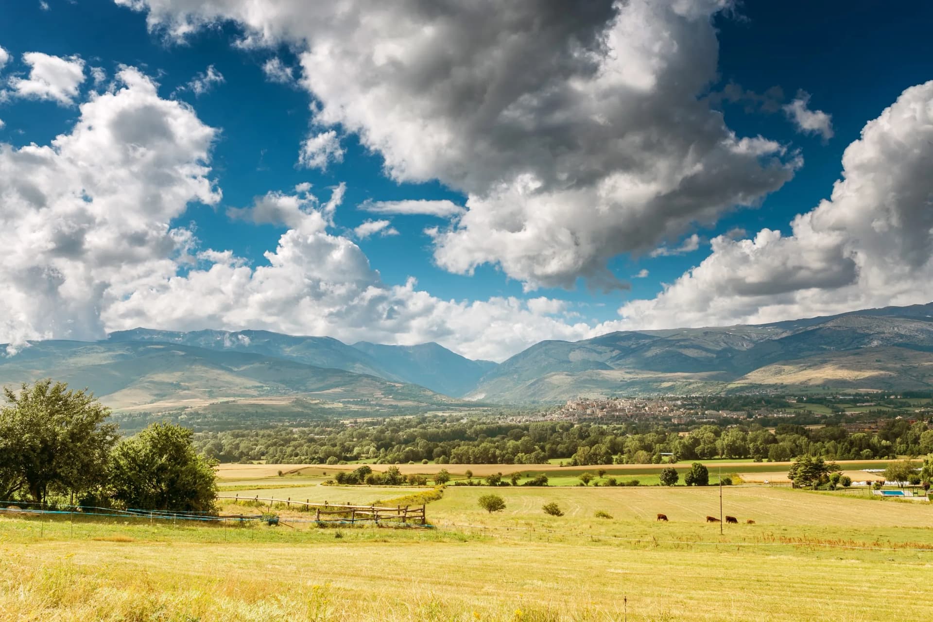 Scenic aerial view of Pyrenees mountain valley with fields, villages, and Puigcerdà under dramatic clouds.