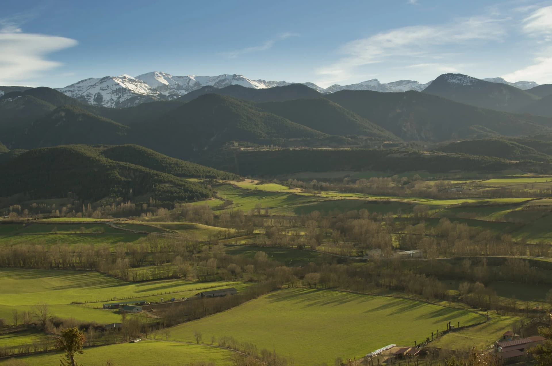 Snowy mountains above green valleys and rolling hills in Bellver de Cerdanya, Catalan Pyrenees, Spain.