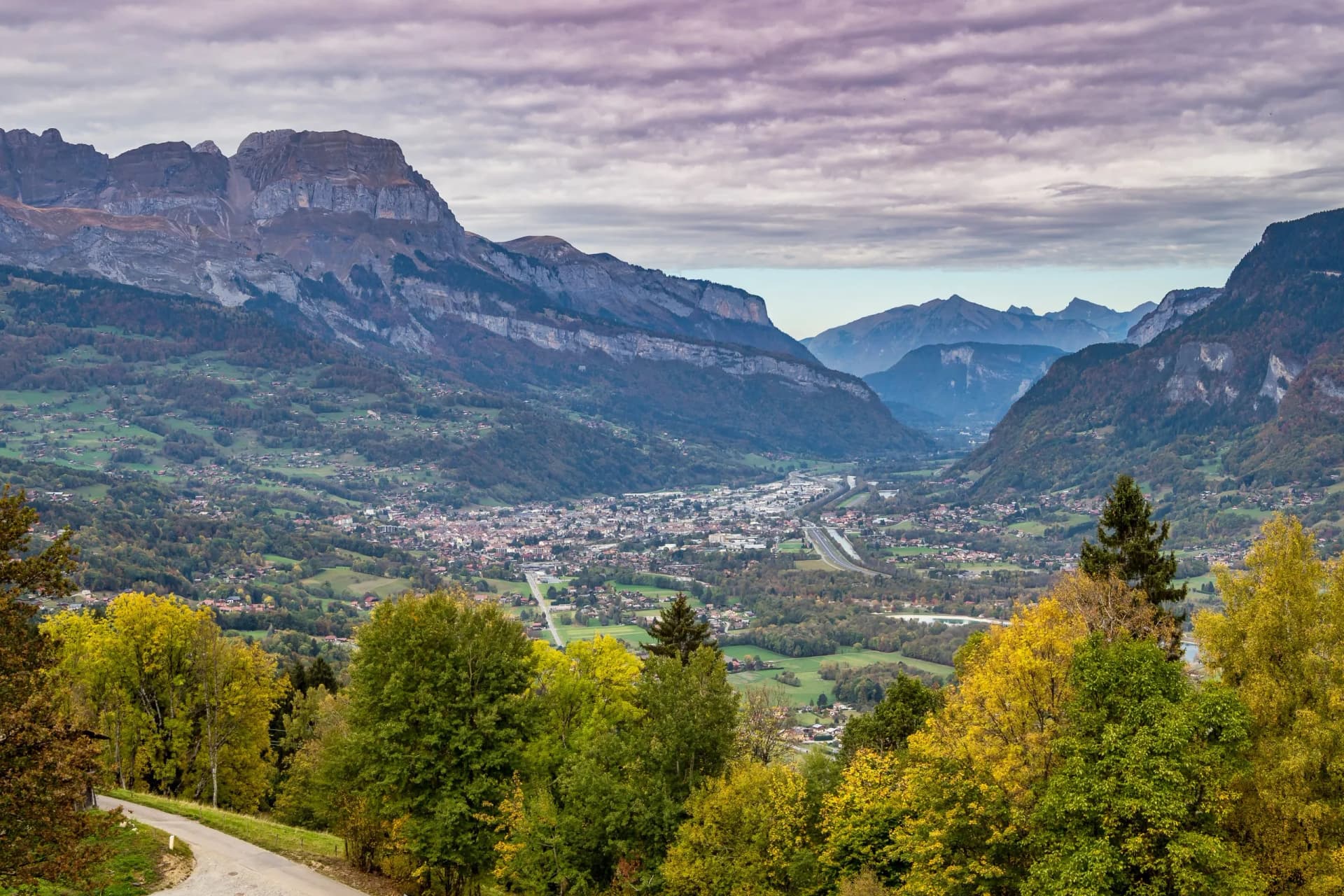 Autumn road near Megève, France, overlooking a valley town and the Haute-Savoie mountains.