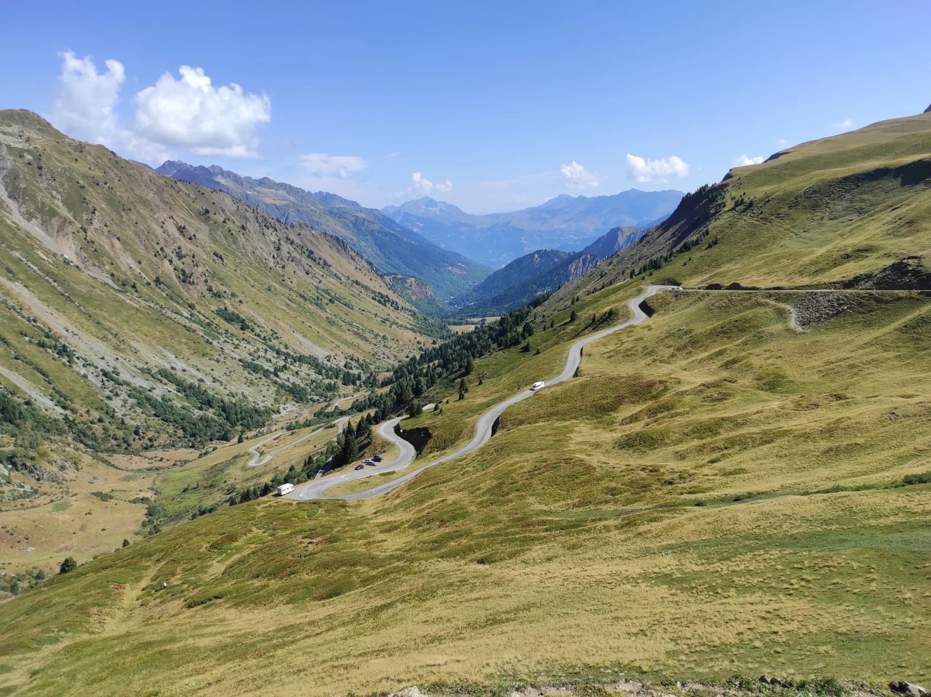 Winding mountain road near Col du Glandon in Savoie, France, surrounded by grassy slopes and distant peaks.