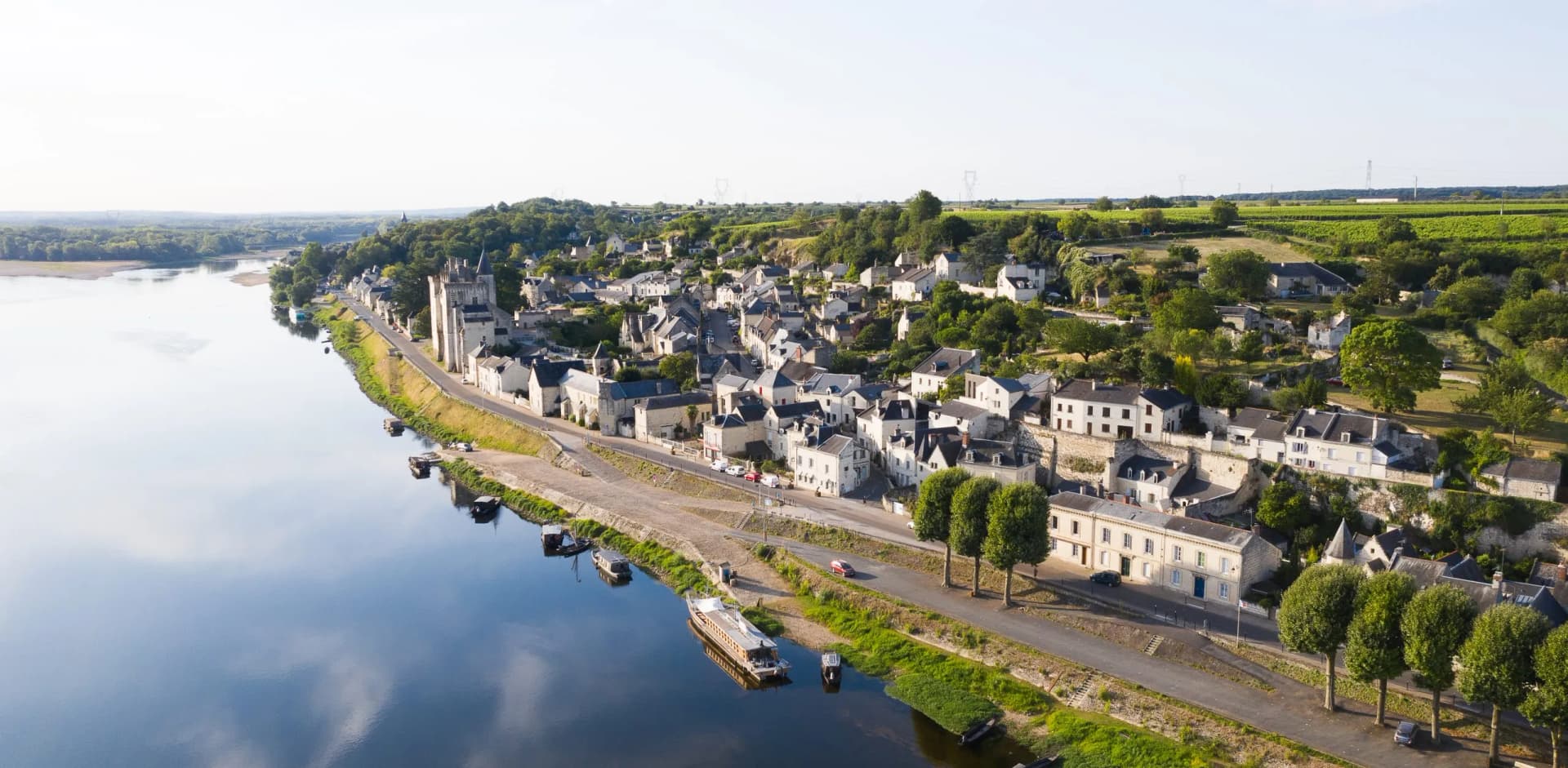 Drone view of Montsoreau village with white buildings along the Loire River and green vineyards.