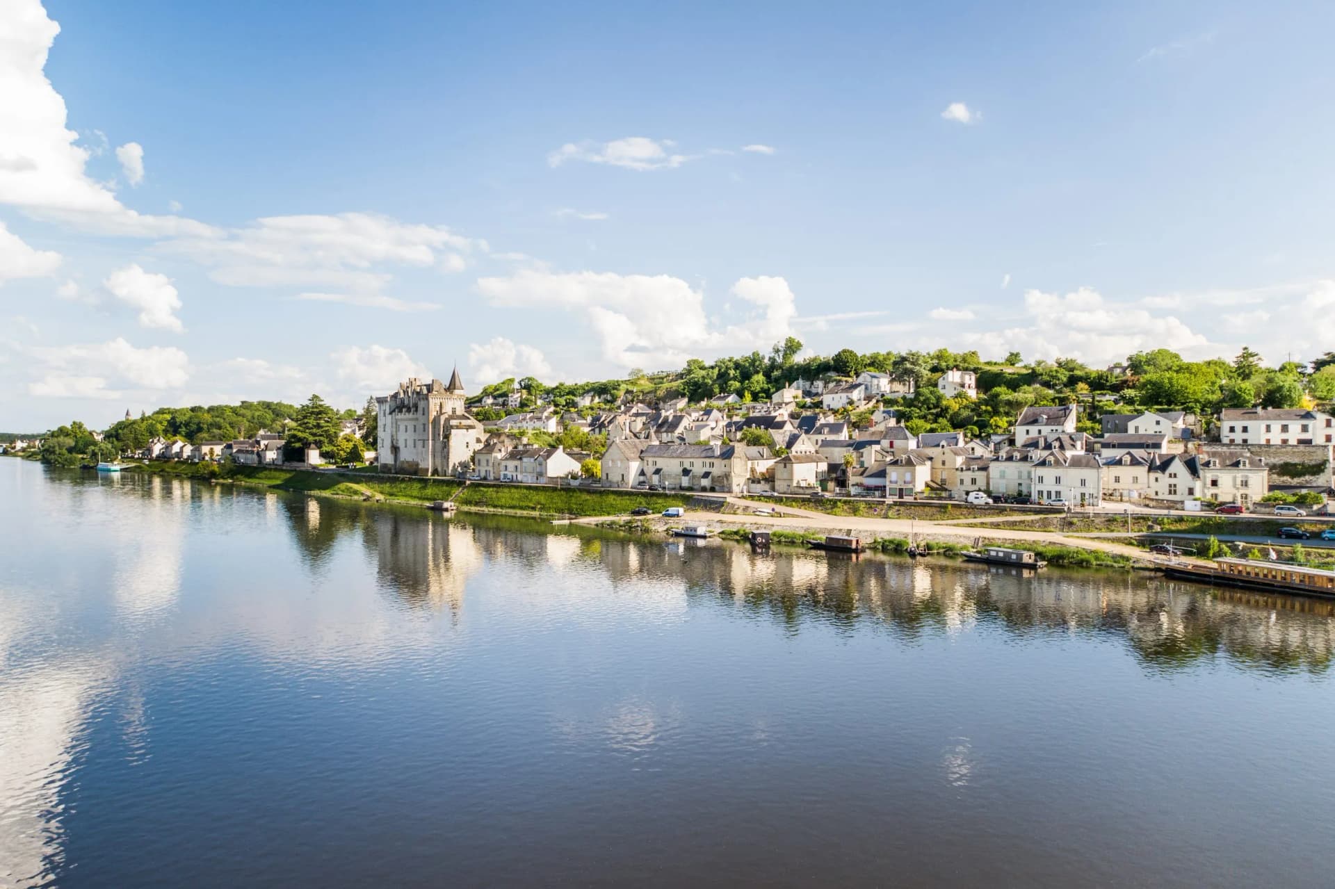 Aerial view of Montsoreau village with chateau on the Loire River, France, under blue sky.