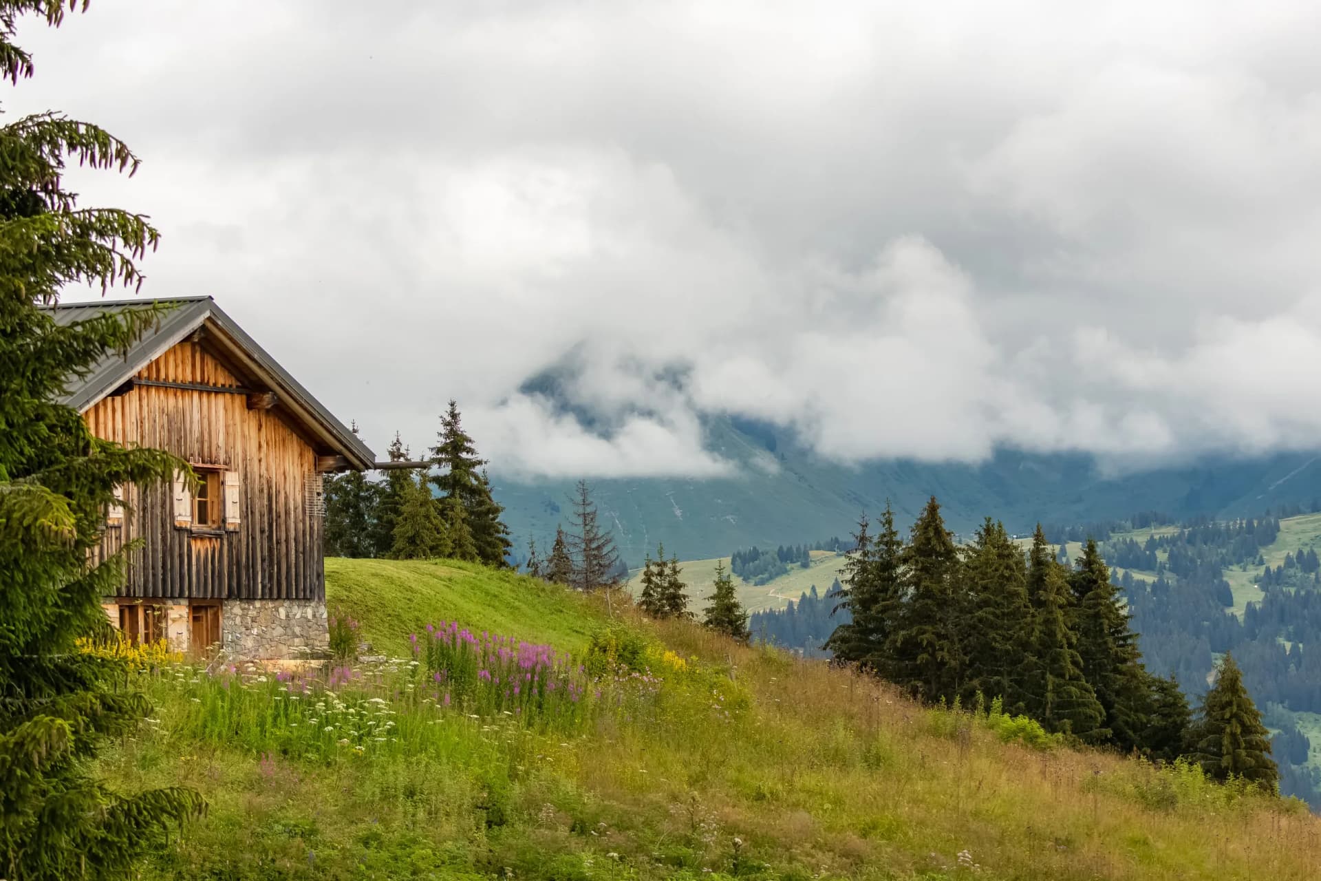 Wooden alpine chalet near Morzine, France, with mountains shrouded in spring clouds.