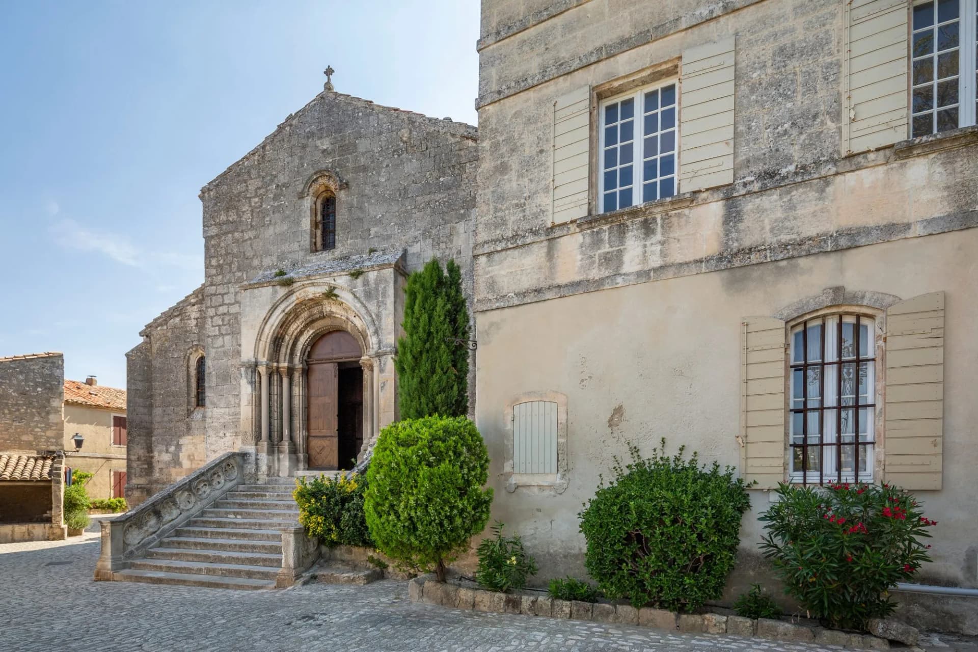 Stone church entrance with arched doorway and steps, next to a stucco building in Les Baux de Provence.