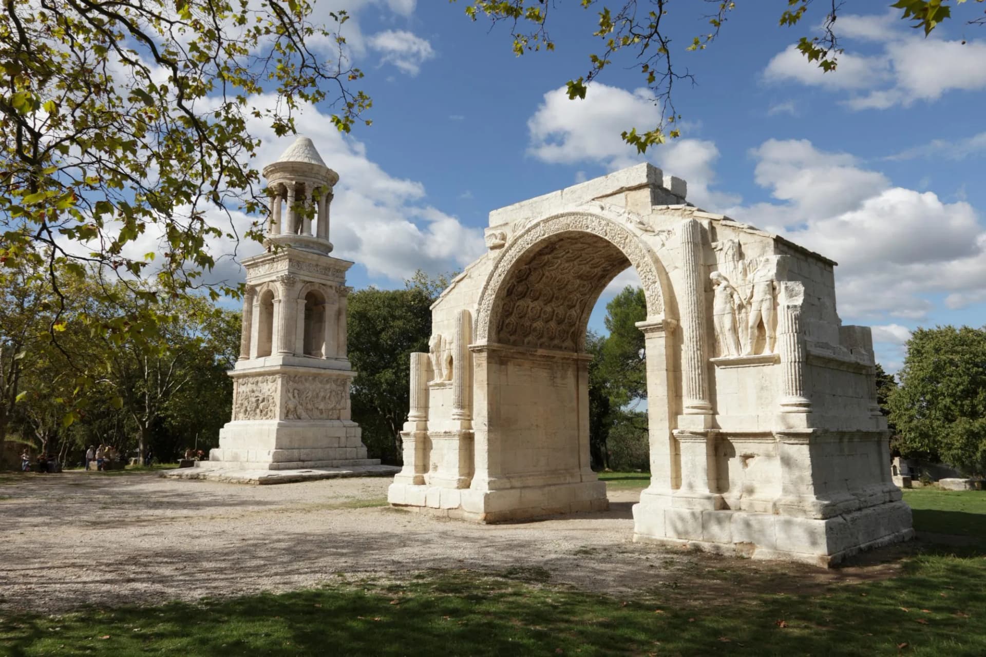 Roman triumphal arch and funerary monument at Glanum Archaeological Park under a blue sky.