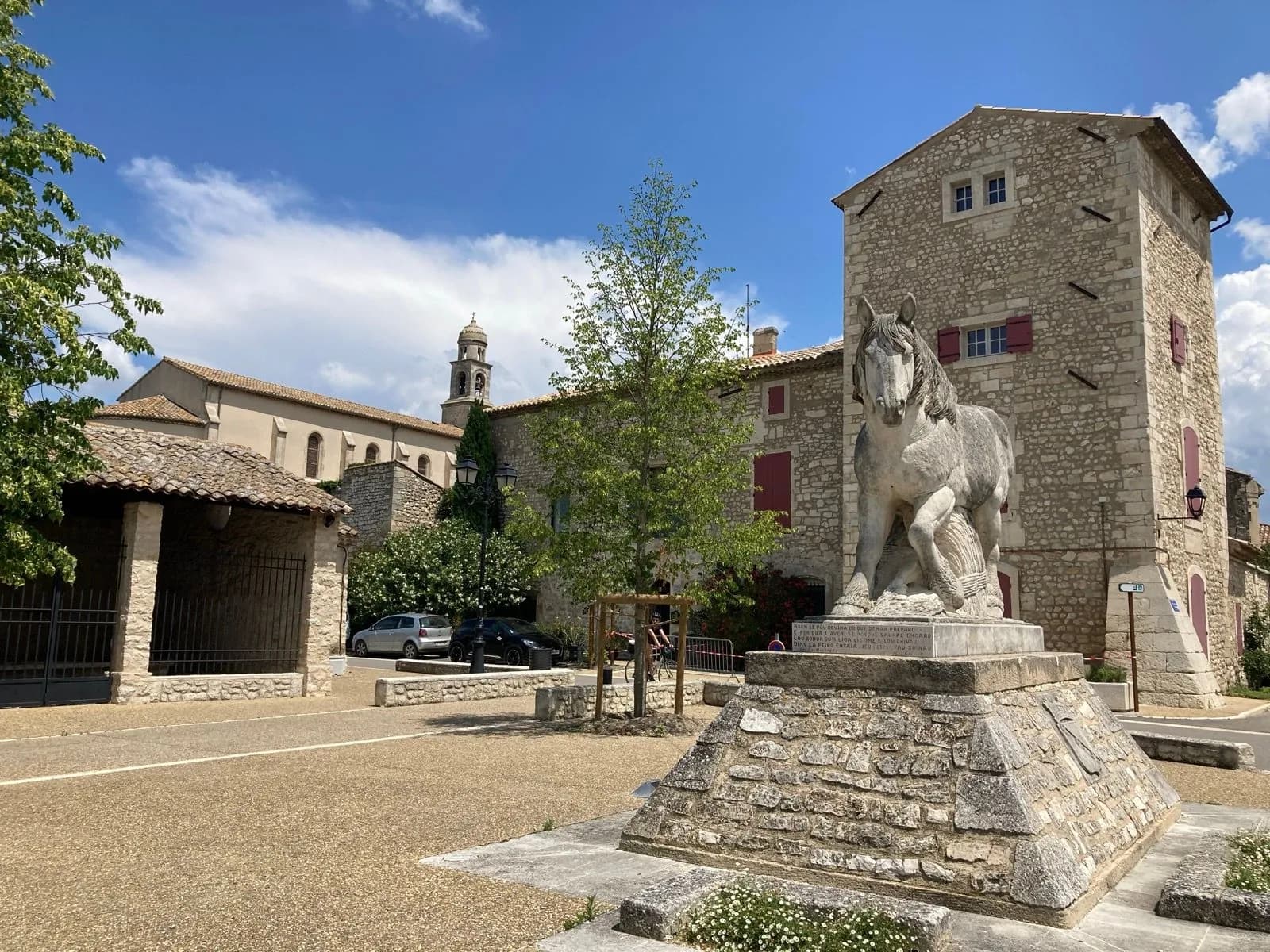 Stone horse monument in square with stone buildings and church tower under blue sky