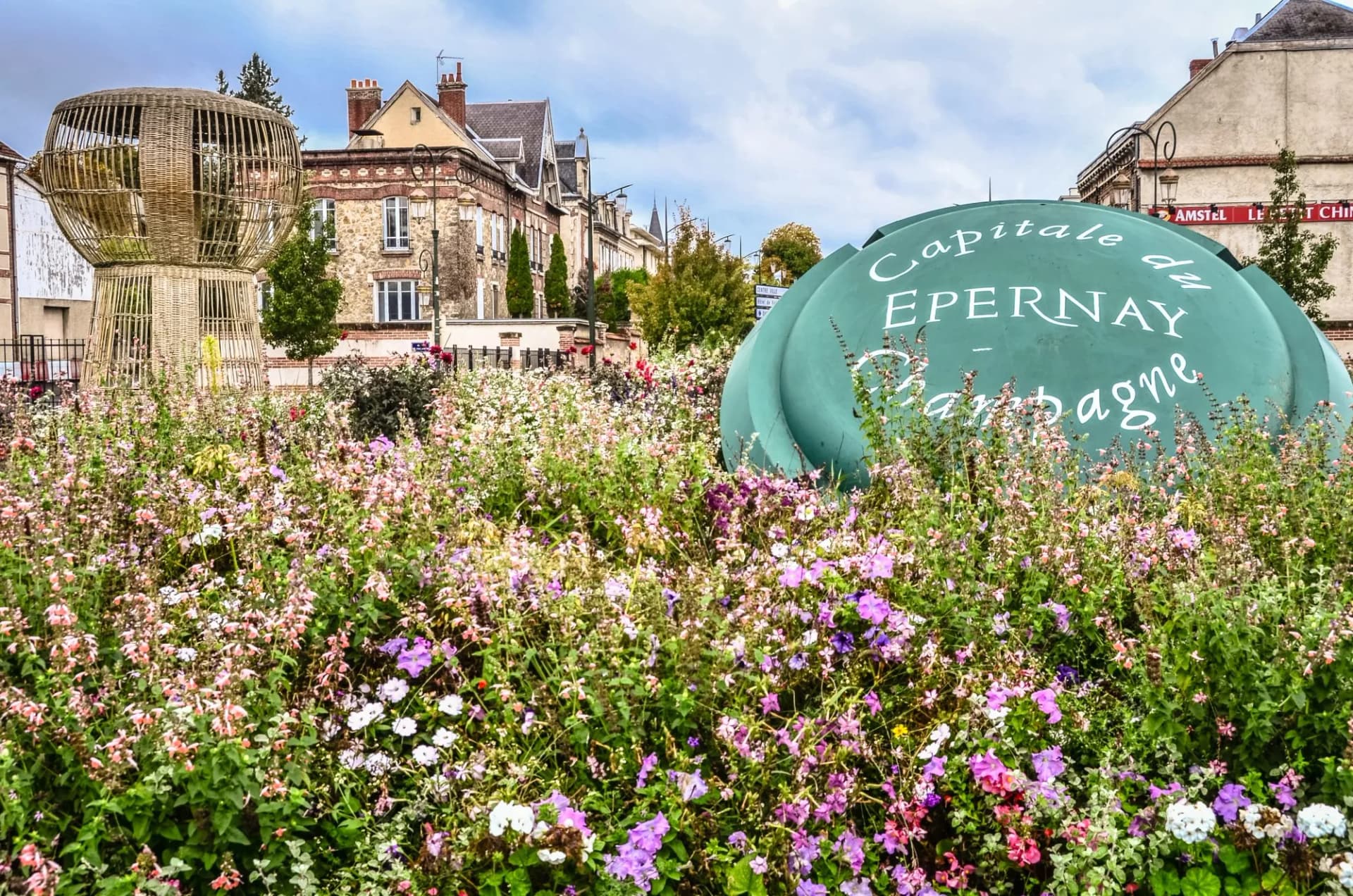 Epernay welcome sign partially visible behind dense flower bed with wicker sculpture and buildings.