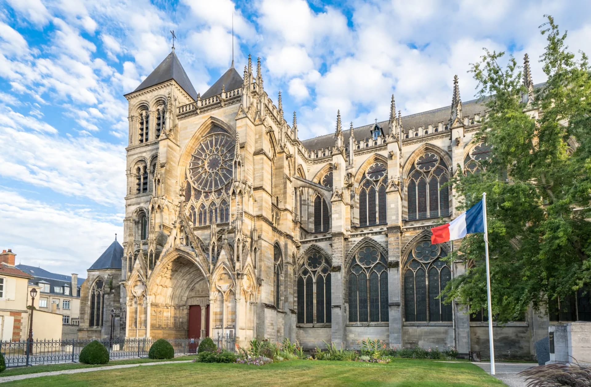 Gothic cathedral exterior with rose window, French flag, and green lawn under blue sky in Chalons.