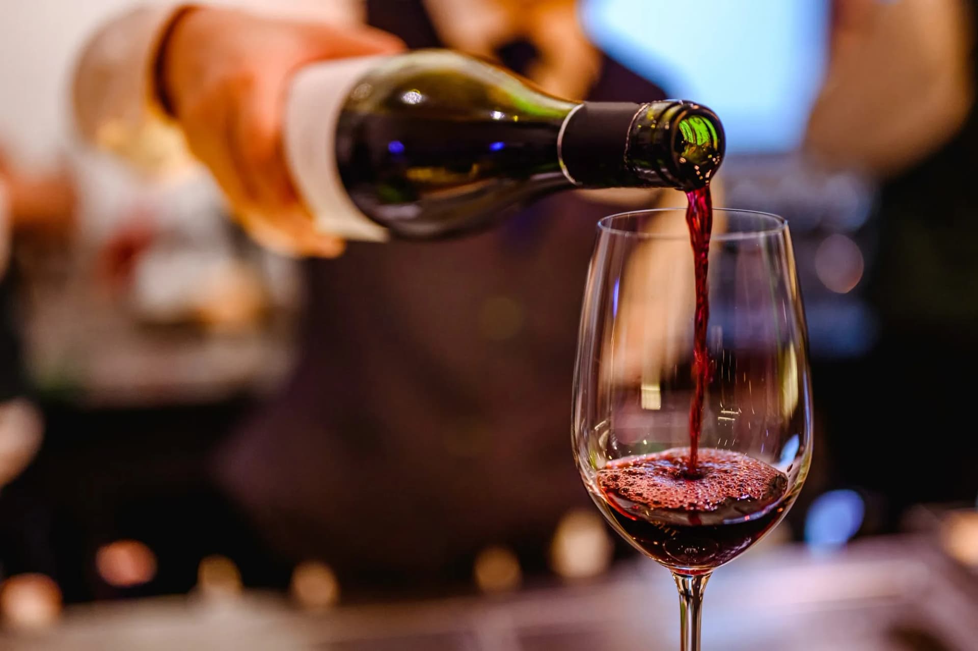 Pouring red wine from a dark bottle into a clear stemmed glass indoors.