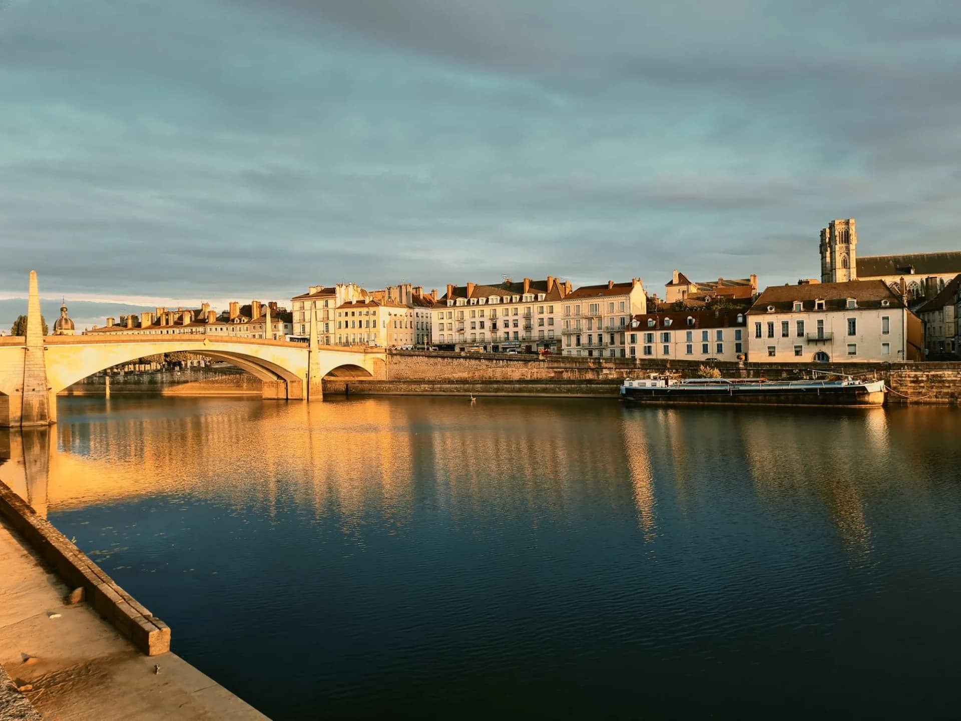 River scene in Chalon with stone bridge, historic buildings, and moored barge at sunset.