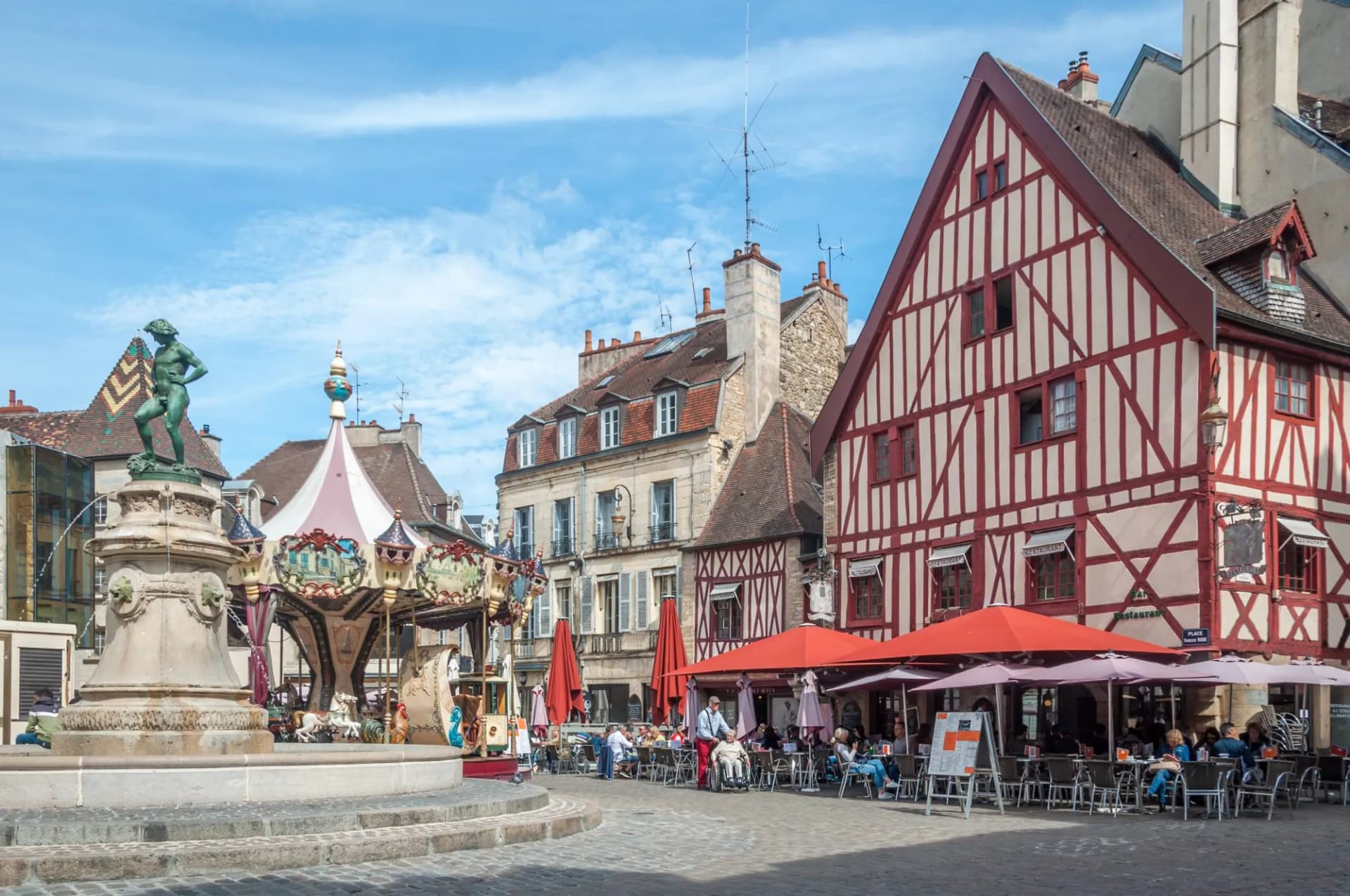 Fountain, carousel, and outdoor cafe seating near half-timbered building in Burgundy.