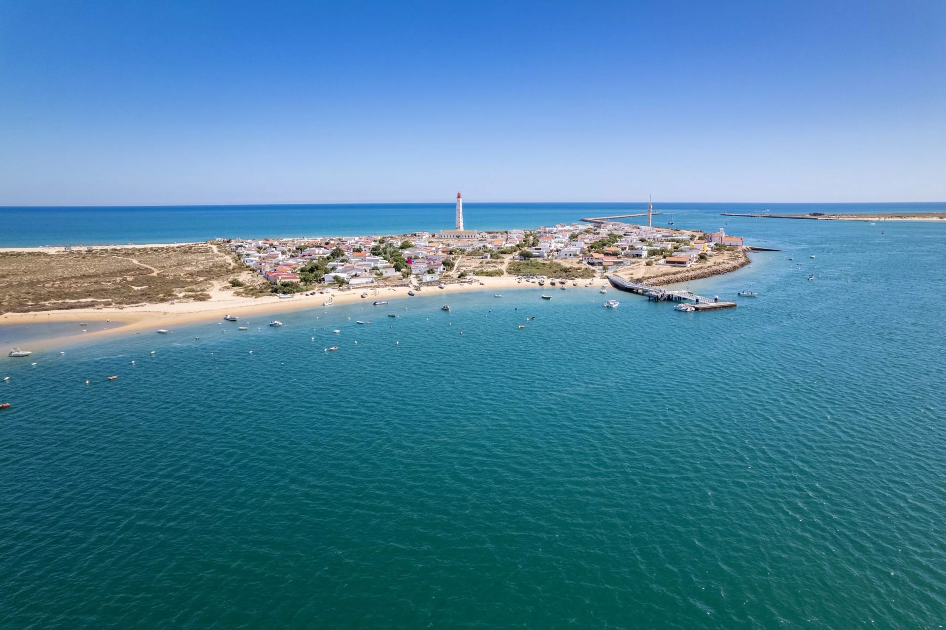 Aerial seascape view of Cape Santa Maria lighthouse island, Praia do Farol beach, one of the barrier islands that protect the Ria Formosa natural park, in Algarve Tourism Destination region, Portugal