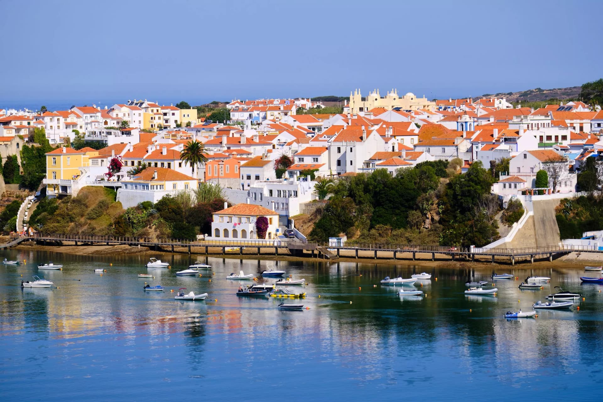 The city Vila Nova de Milfontes is reflected in the waters of the harbor full of boats. Solo Backpacker Trekking on the Rota Vicentina and Fishermen's Trail in Alentejo, Portugal. Walking between clif