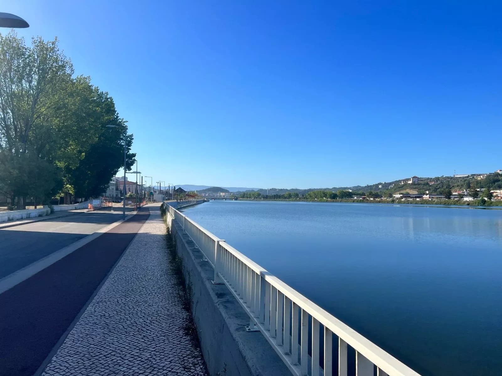 Cobblestone cycle path beside river near Coimbra with clear blue sky.