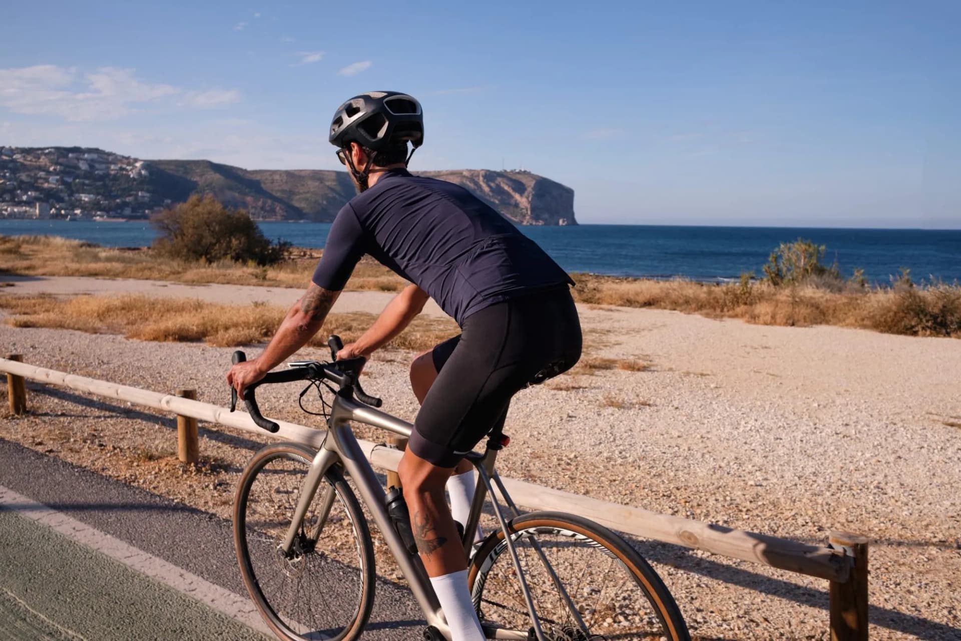 Cyclist riding road bike along dry coastal path with sea and cliffs in background