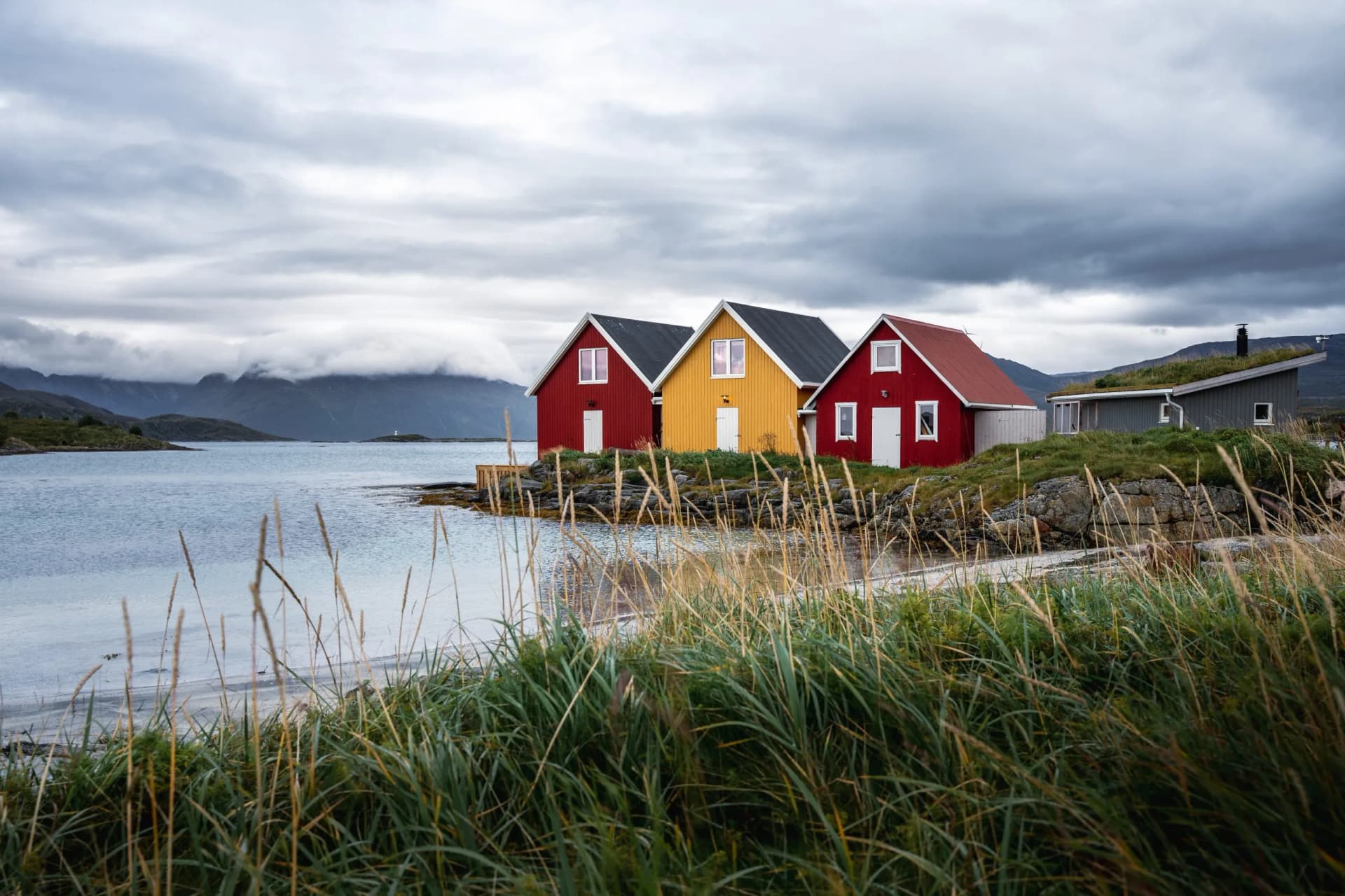 Colorful waterfront cabins in Sommarøy against a backdrop of cloudy mountains and sea.