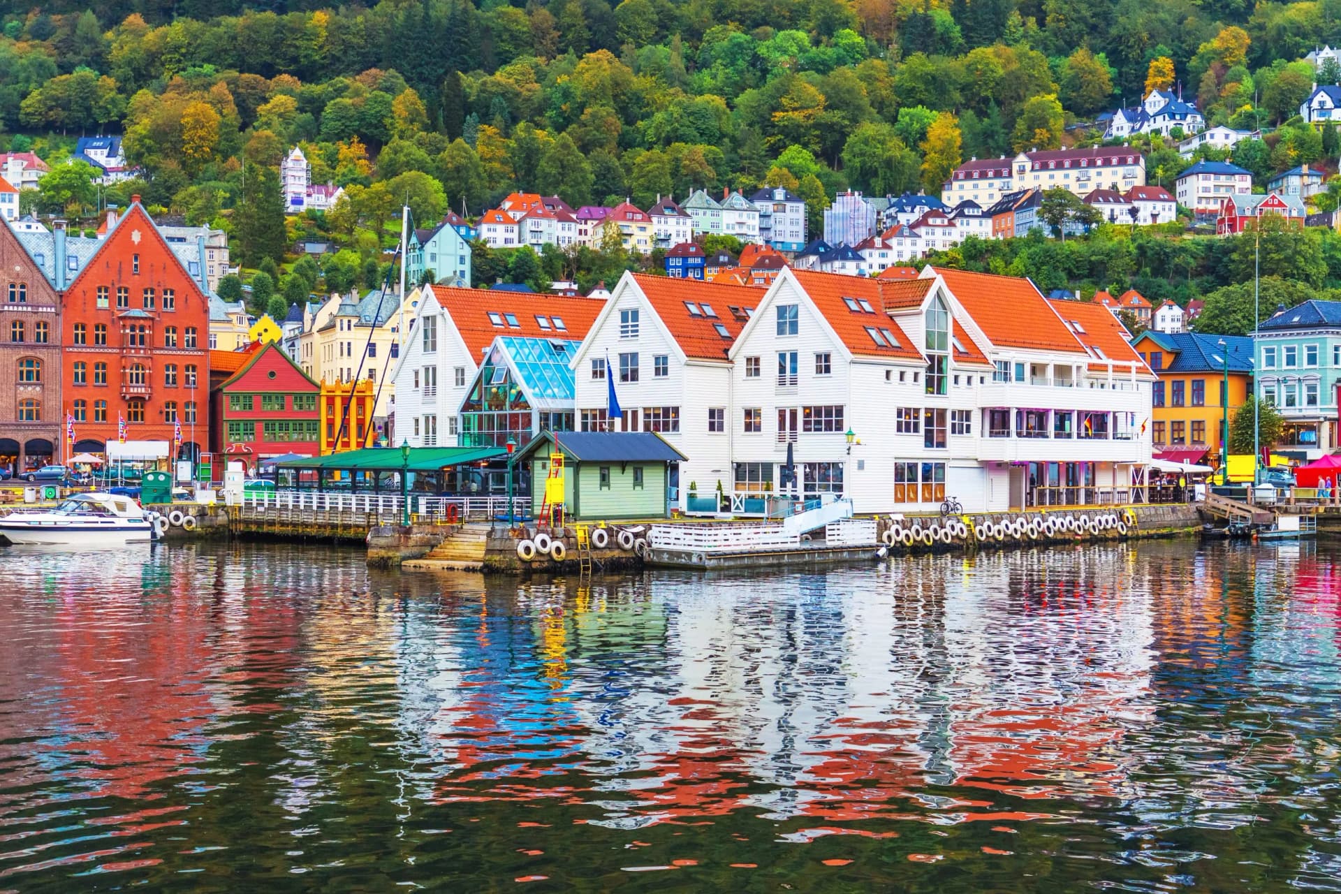 Colorful waterfront buildings in Bergen reflected in the harbor water with forested hillsides.