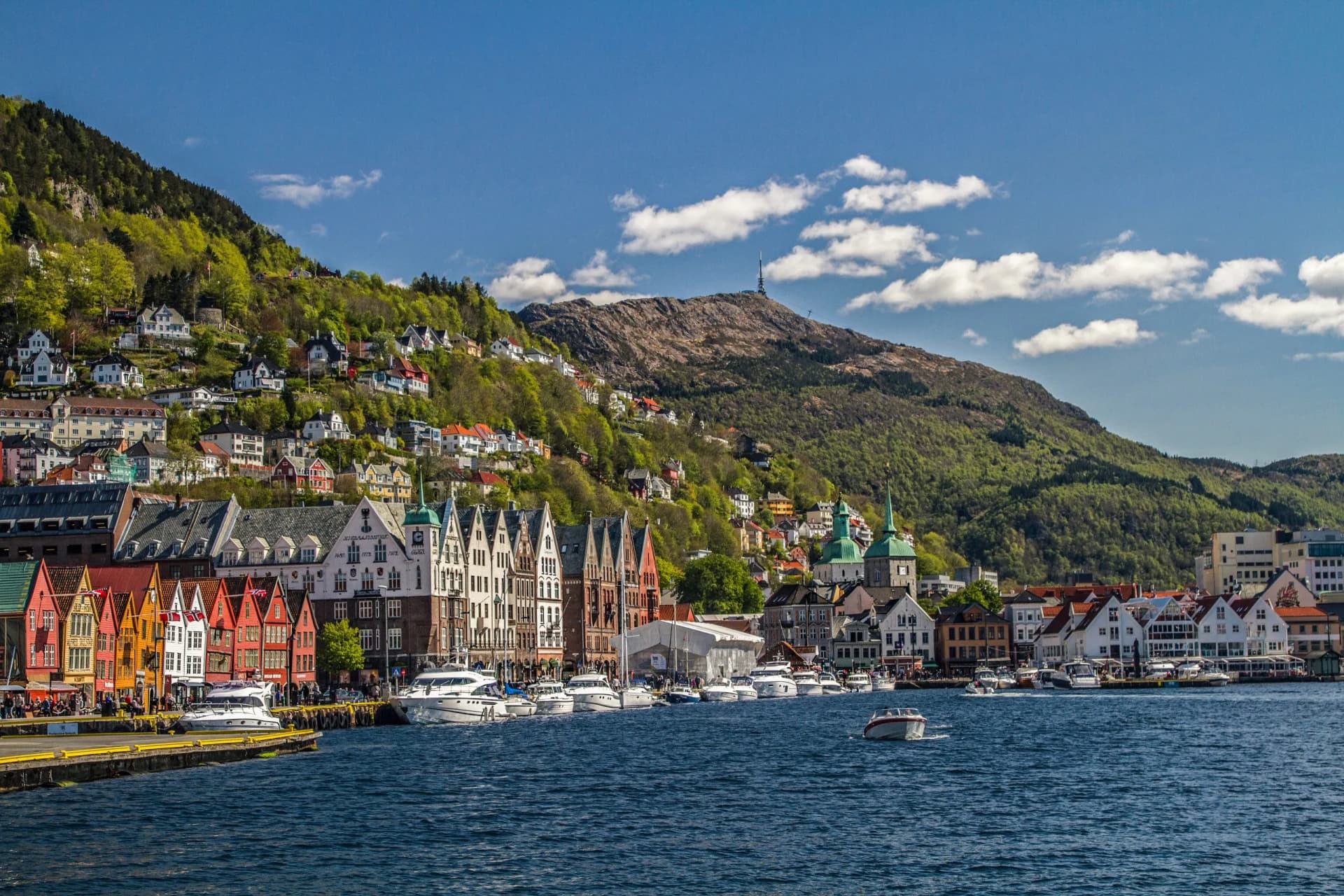Colorful Bryggen wharf houses in Bergen Norway with boats on the harbor and green mountains.