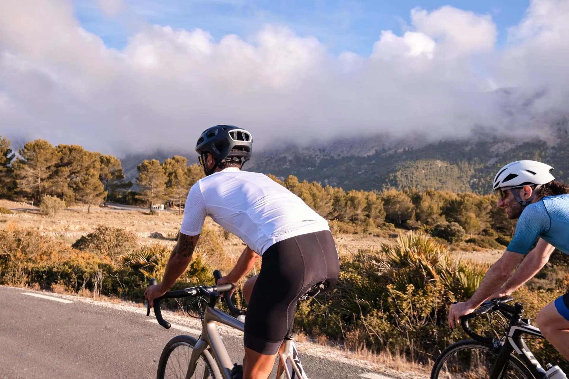 Cyclists in full cycling gear and helmets ride their road bikes on mountain road at sunset. Sportsmen training hard on bicycle outdoors. Spain