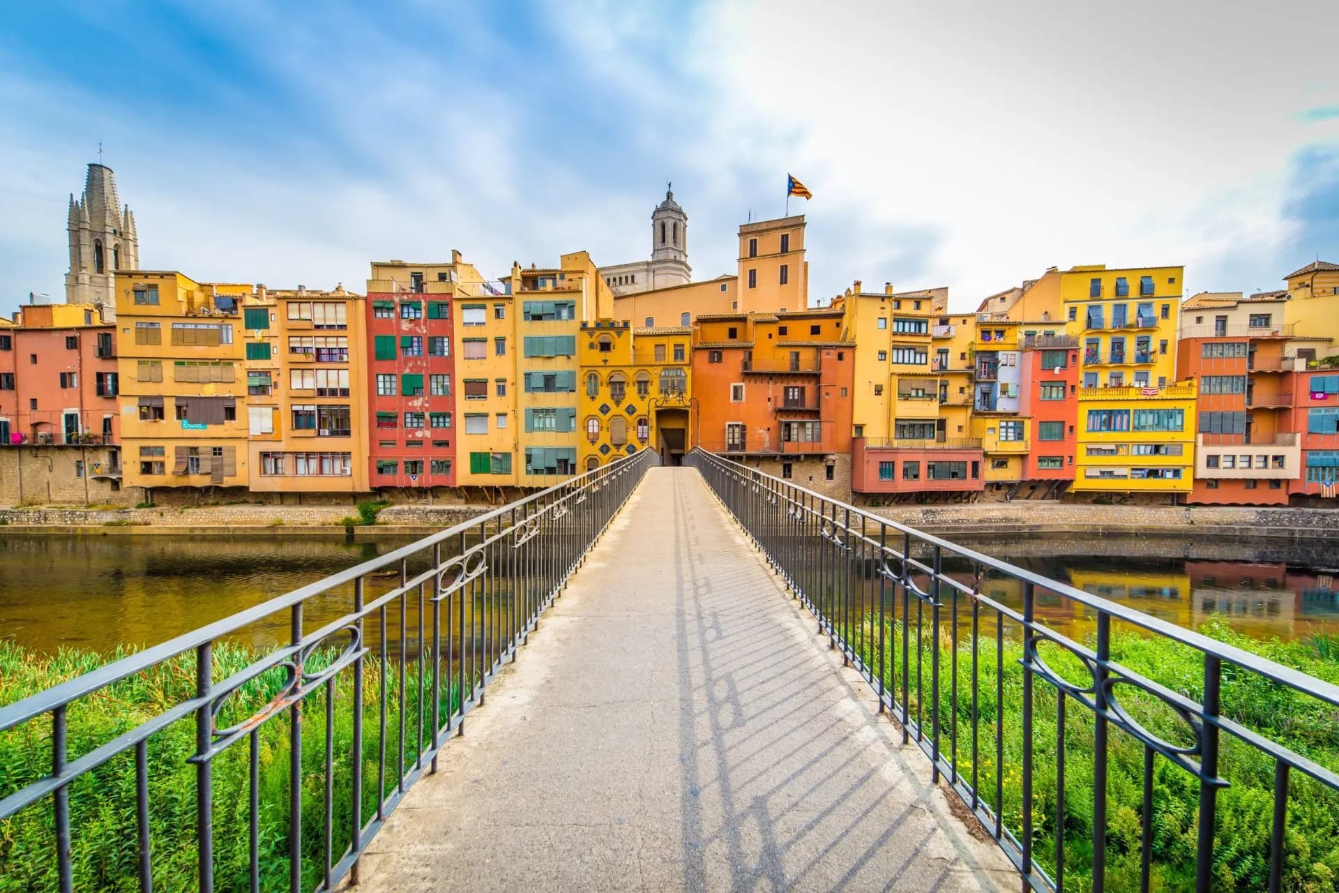Footbridge leading to colorful riverside buildings and cathedral in Girona, Spain.