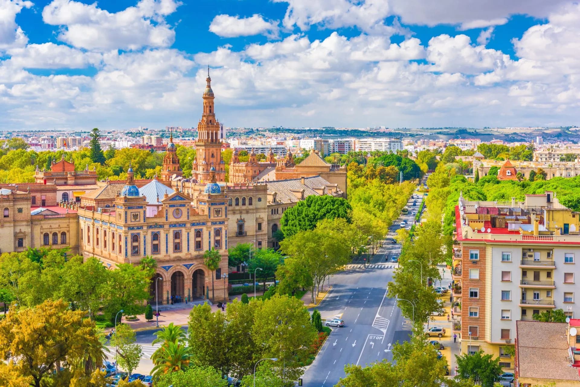 Plaza de España building in Seville, Spain, with tree-lined avenue and city skyline under blue sky.