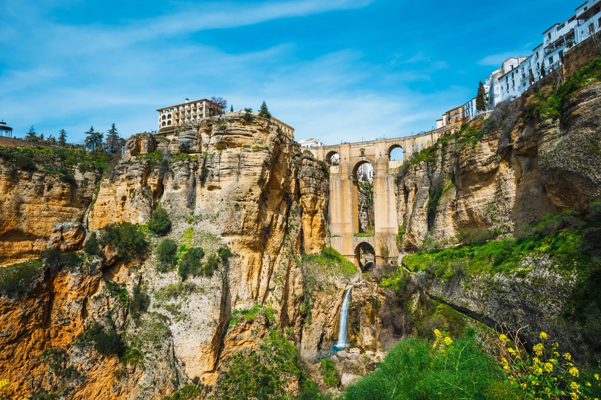 Stone bridge over gorge with waterfall, white buildings on cliffs, Ronda, Andalusia, Spain.