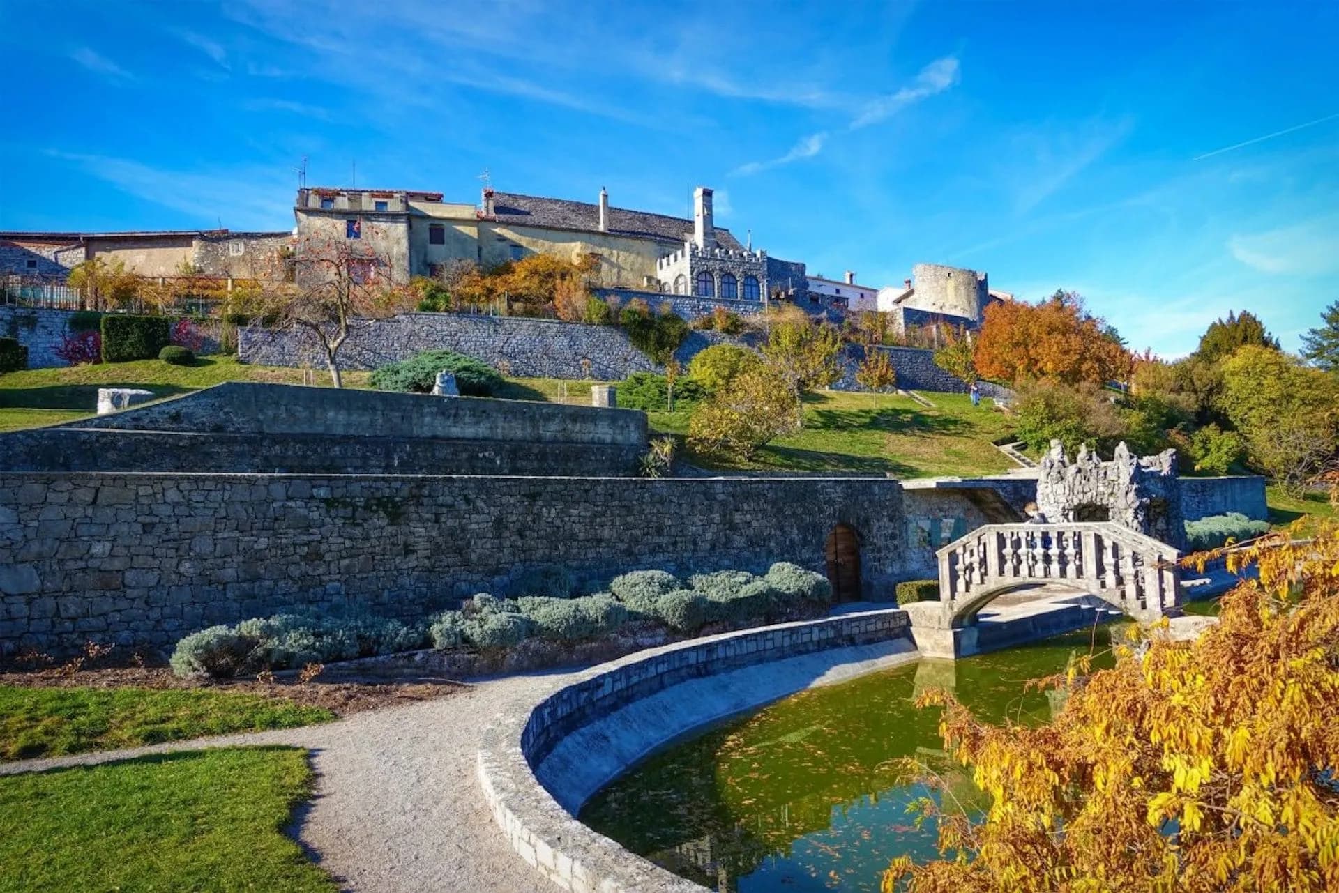 Stanjel castle complex overlooking terraced gardens and a small bridge over a pond in autumn.