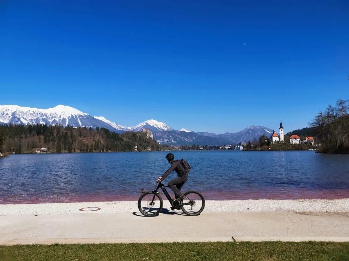 Cyclist by Lake Bled with snow-capped mountains and island church in background
