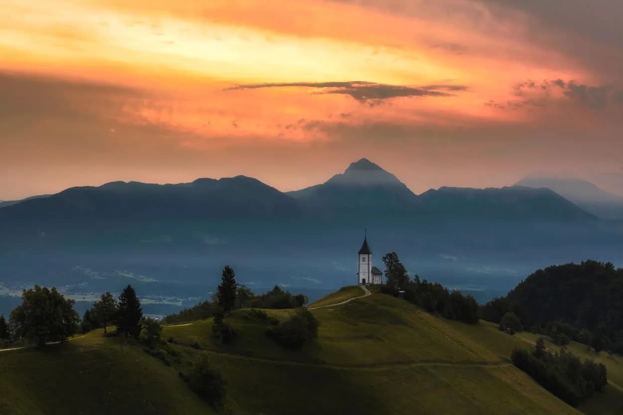 Church on a hilltop overlooking mountains at sunset in Jamnik, Slovenia.