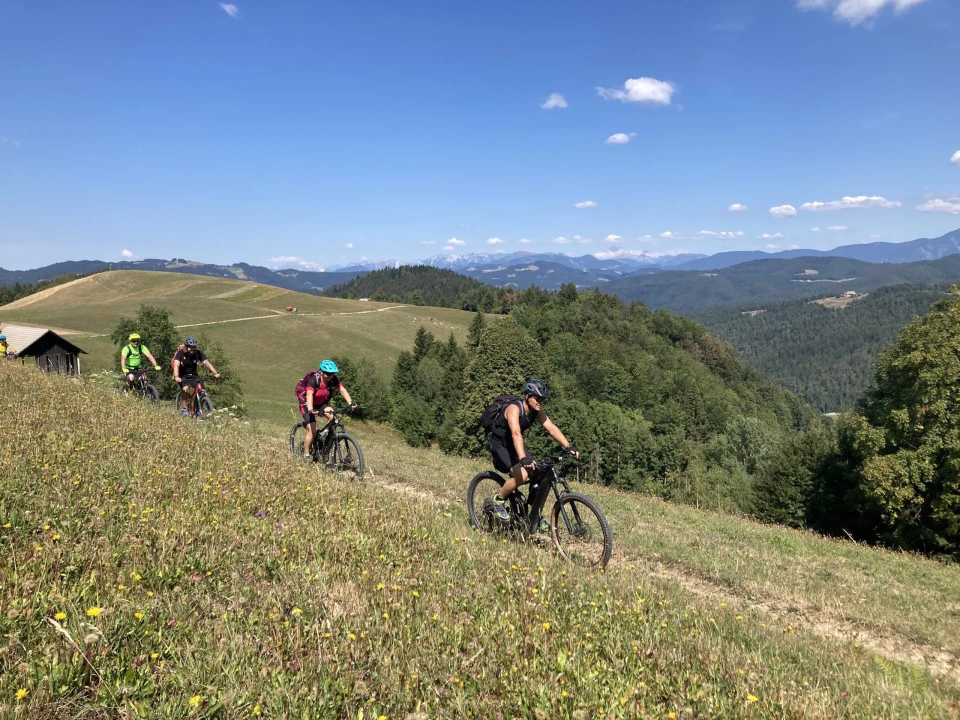 Mountain bikers cycling along a grassy ridge trail overlooking hills near Ziri town.