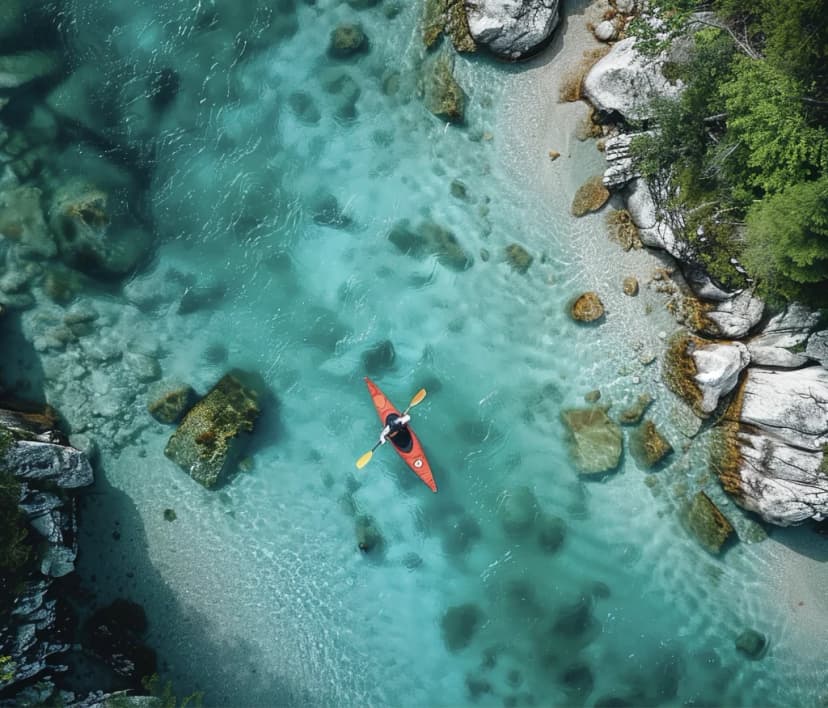 Kayaking in bright turquoise river water with rocky banks and green trees, aerial view.