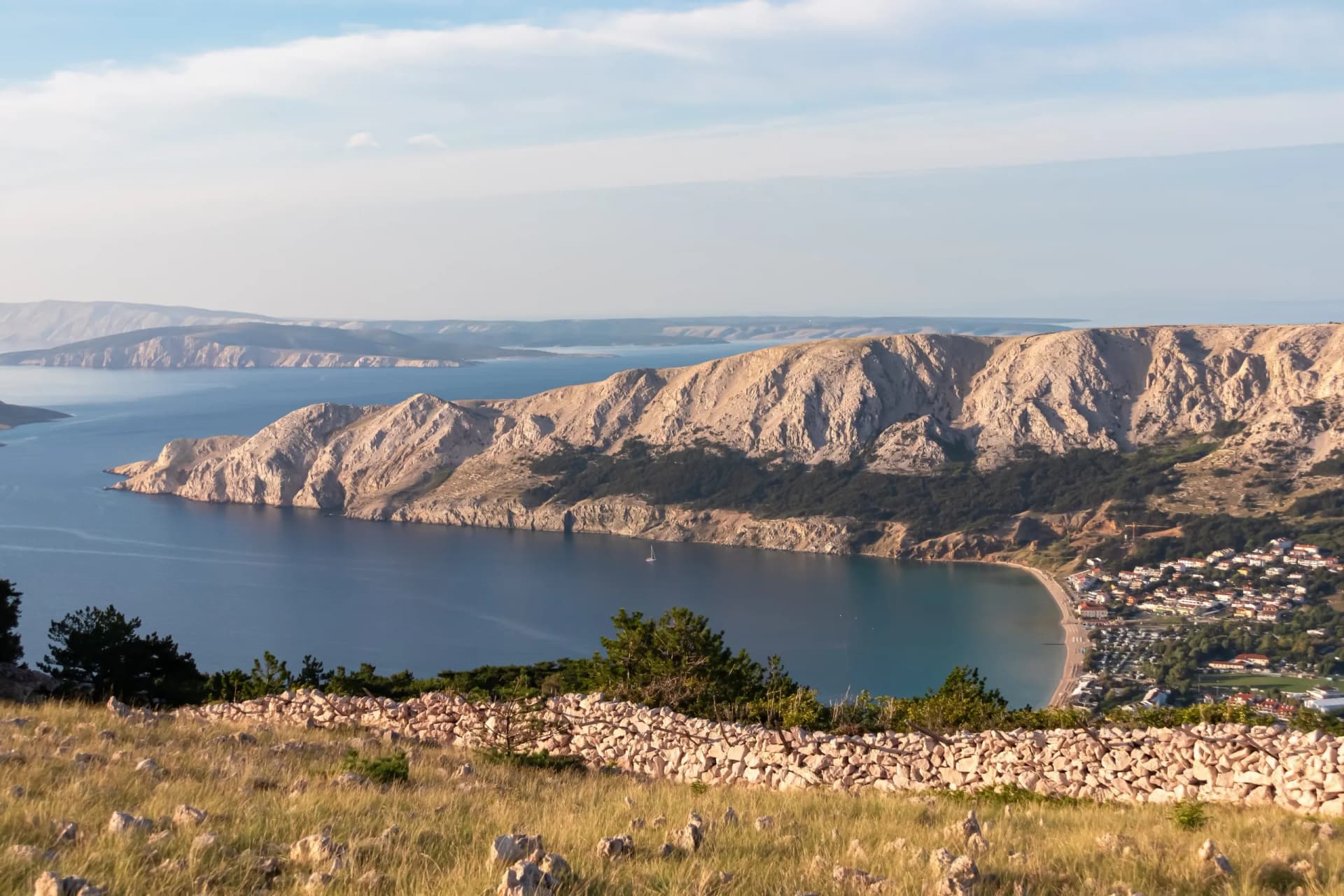 Aerial view of idyllic coastal town Baska, Krk Island, Primorje-Gorski Kotar, Croatia, Europe. Coastline of Adriatic Sea surrounded by karst mountains. Archipelago Kvarner Bay. Path to moon plateau