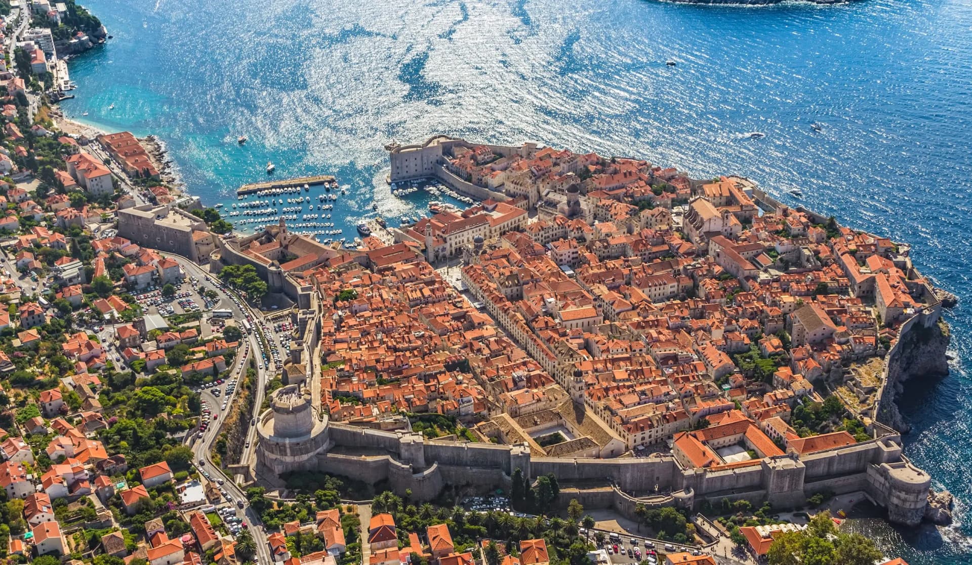 Aerial view of Dubrovnik Old Town walls, terracotta roofs, and sparkling blue Adriatic Sea.