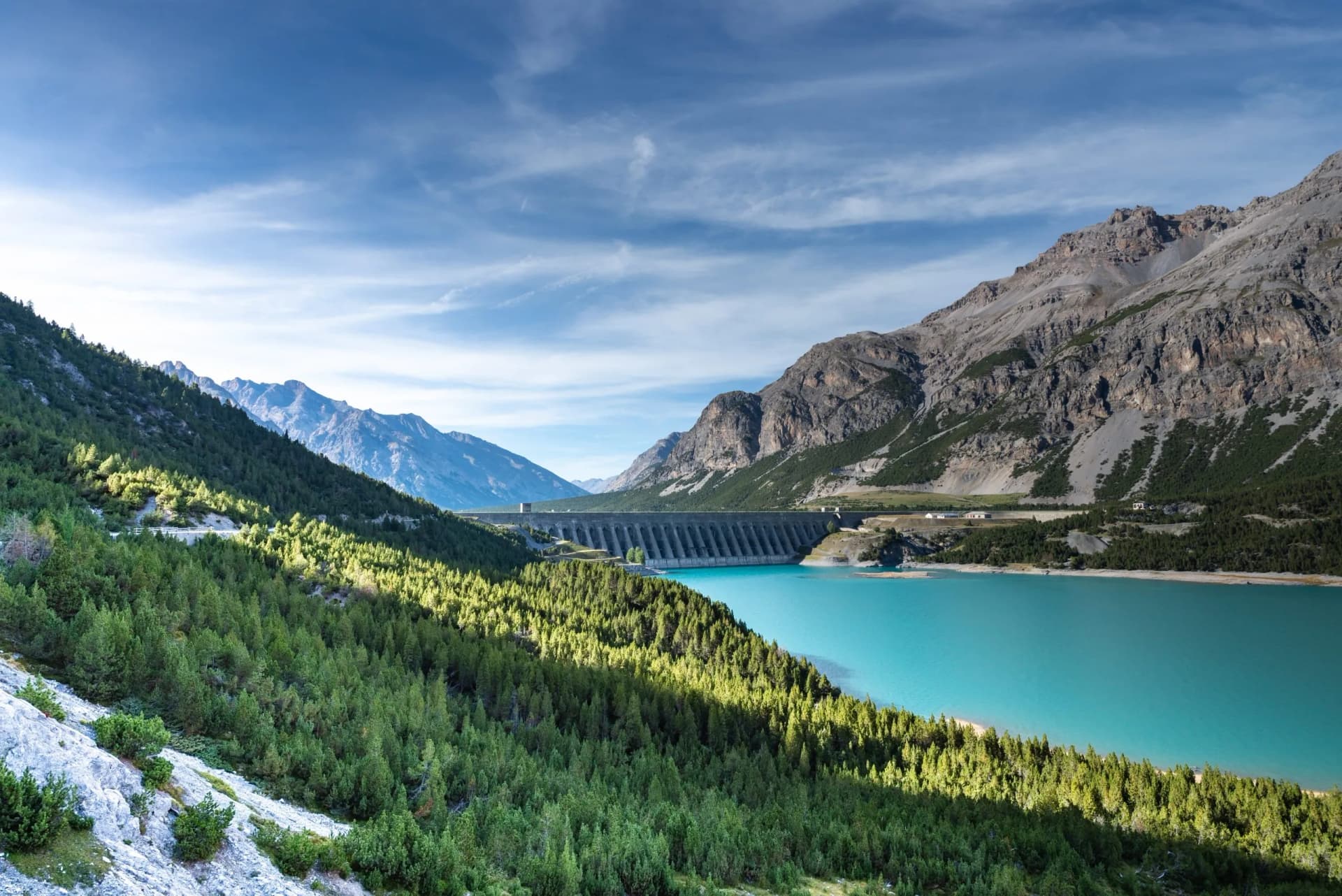 Large dam holding back turquoise water of Lago di Cancano reservoir surrounded by steep mountains.