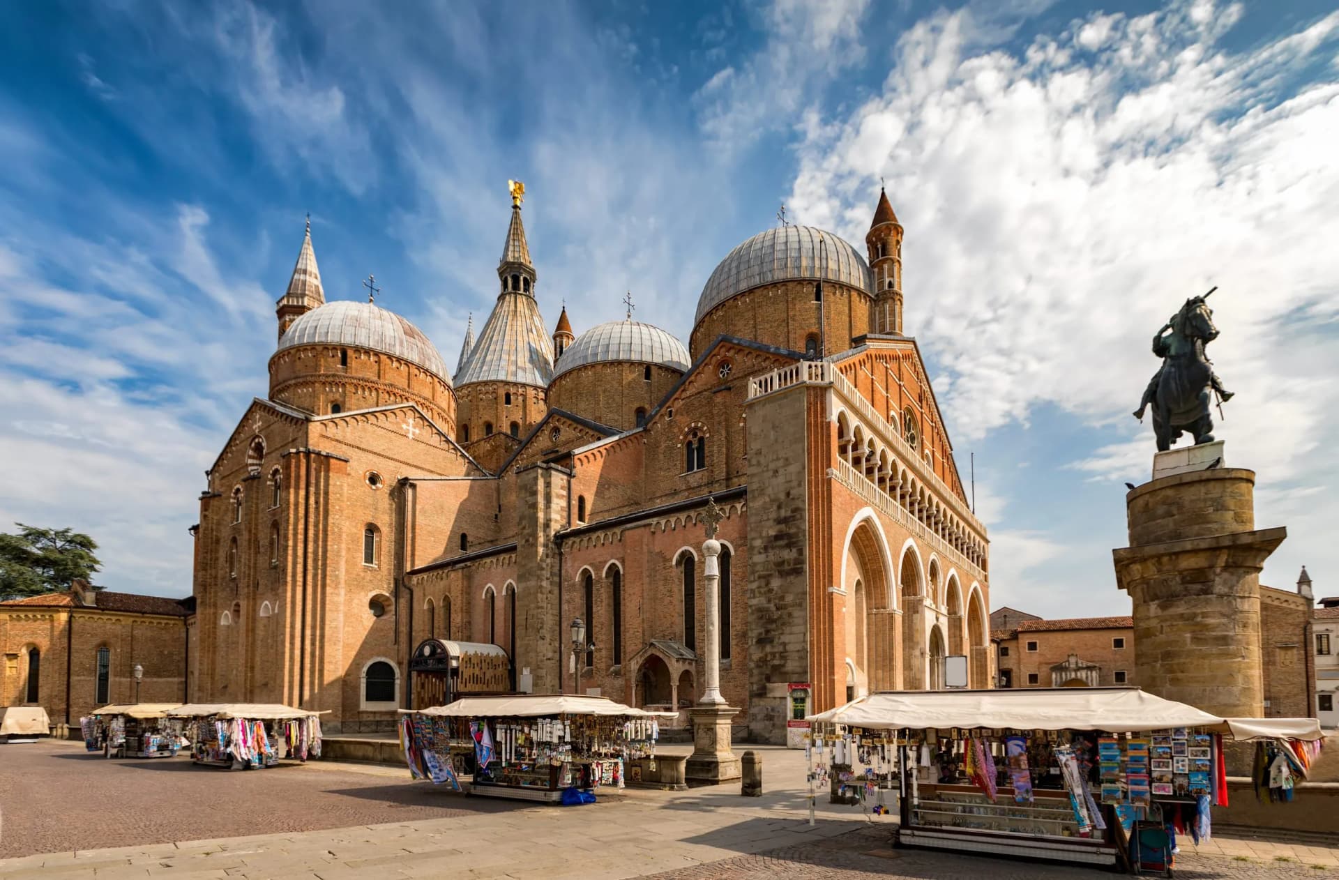 Basilica of Saint Anthony with domes, equestrian statue, and souvenir stalls in Padua.