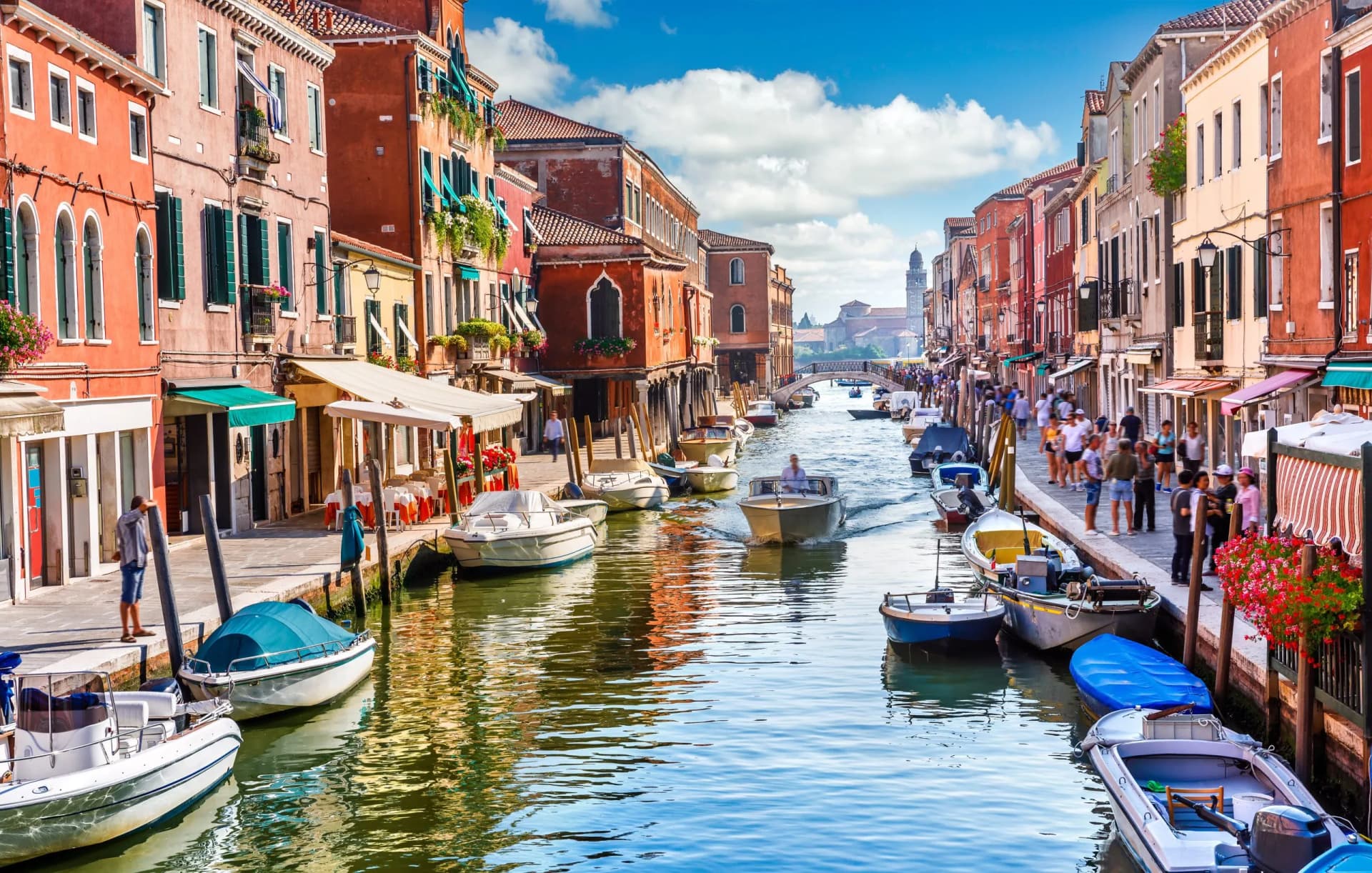 Boats navigating a narrow canal lined with colorful buildings under a bright blue sky in Venice.