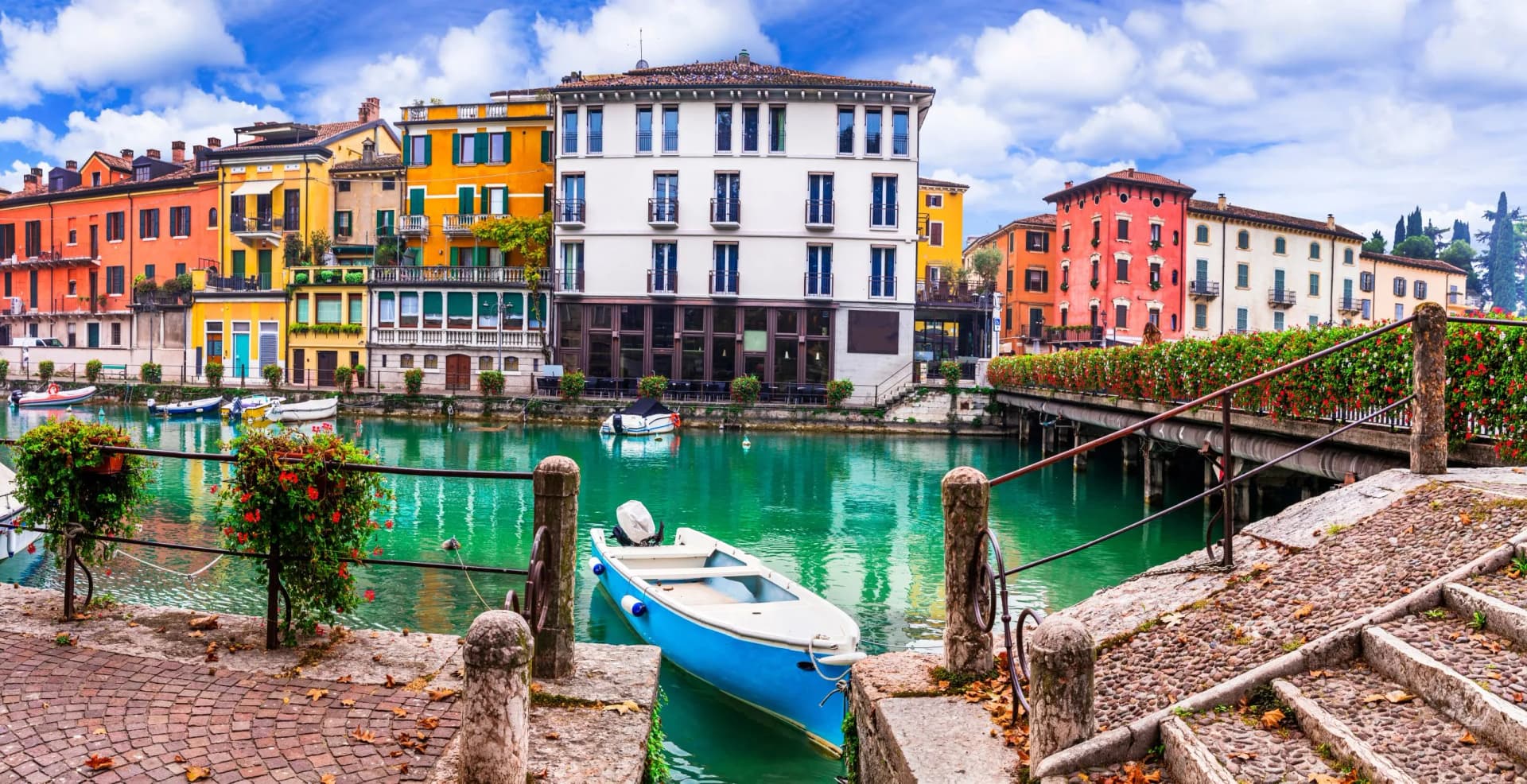 Blue boat moored on canal next to colorful buildings in Peschiera under blue sky.