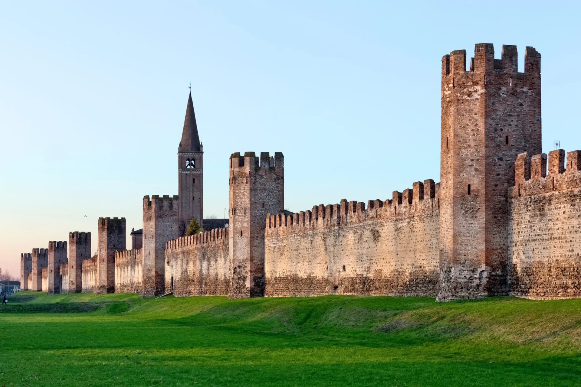 Medieval defensive wall with crenelated towers and a tall spire church in Montagnana, Italy.