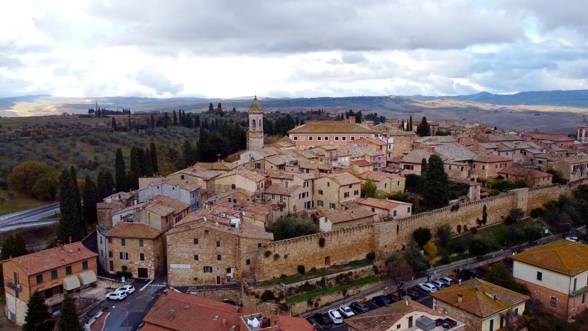 Hilltop town of San Quirico d'Orcia with stone walls, terracotta roofs, and rolling Tuscan landscape.