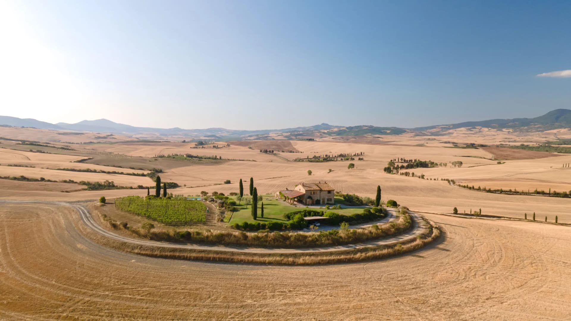 Farmhouse surrounded by cypress trees in rolling golden fields of Val d'Orcia, Tuscany.